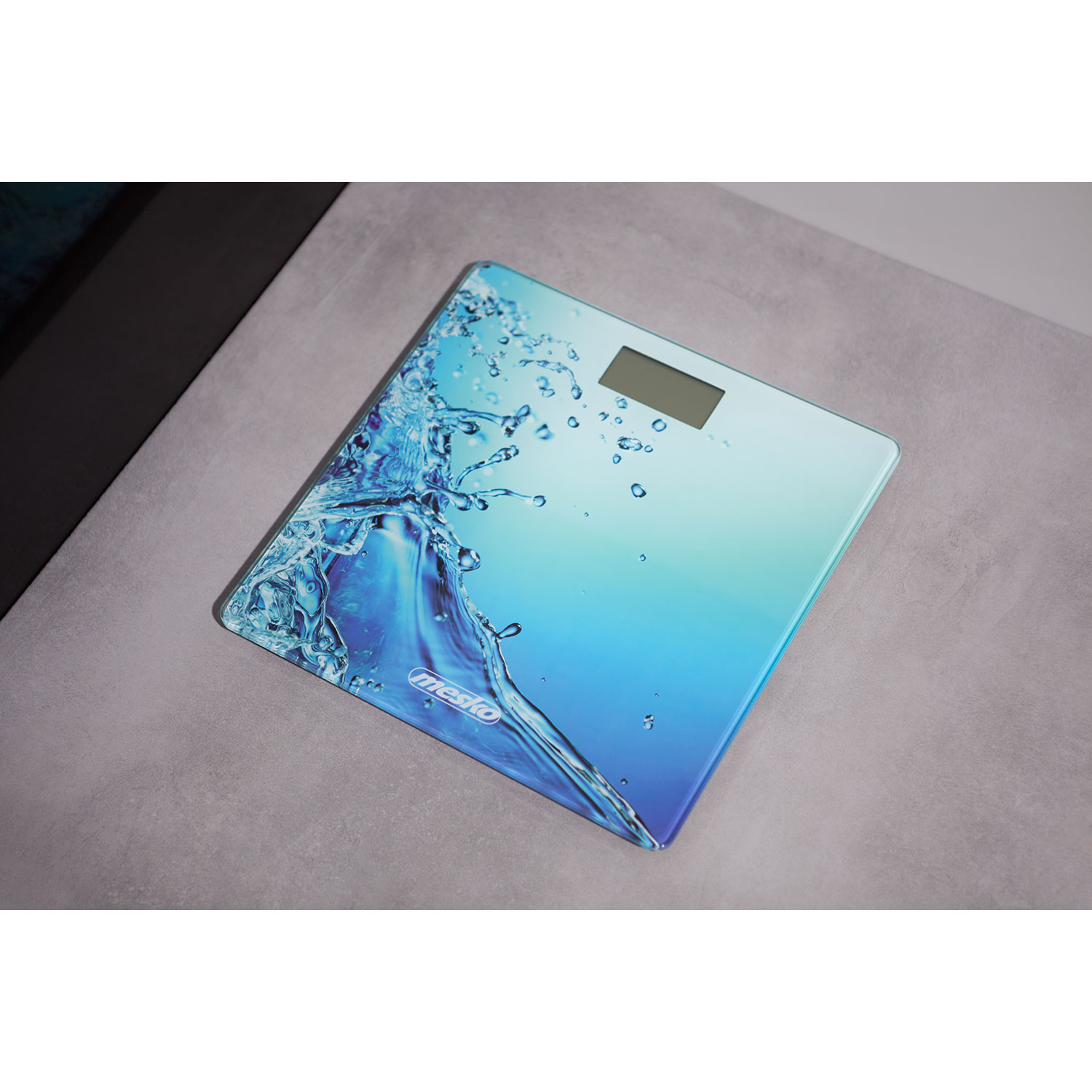 Bilancia da bagno digitale con un design ad acqua blu e turchese. Si trova su una superficie grigia.