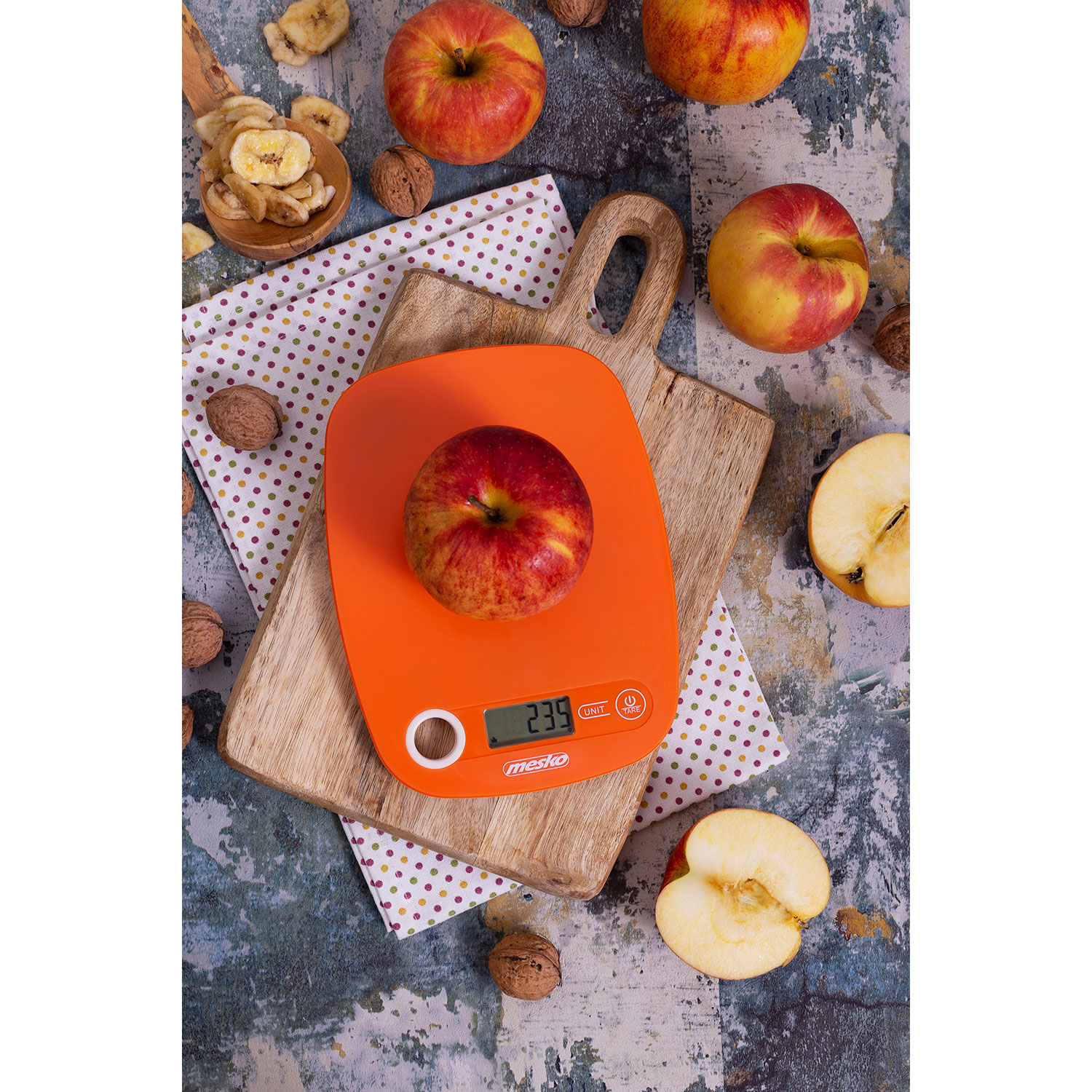 Manzana en una báscula digital sobre una tabla de madera con nueces, fruta seca y manzanas.
