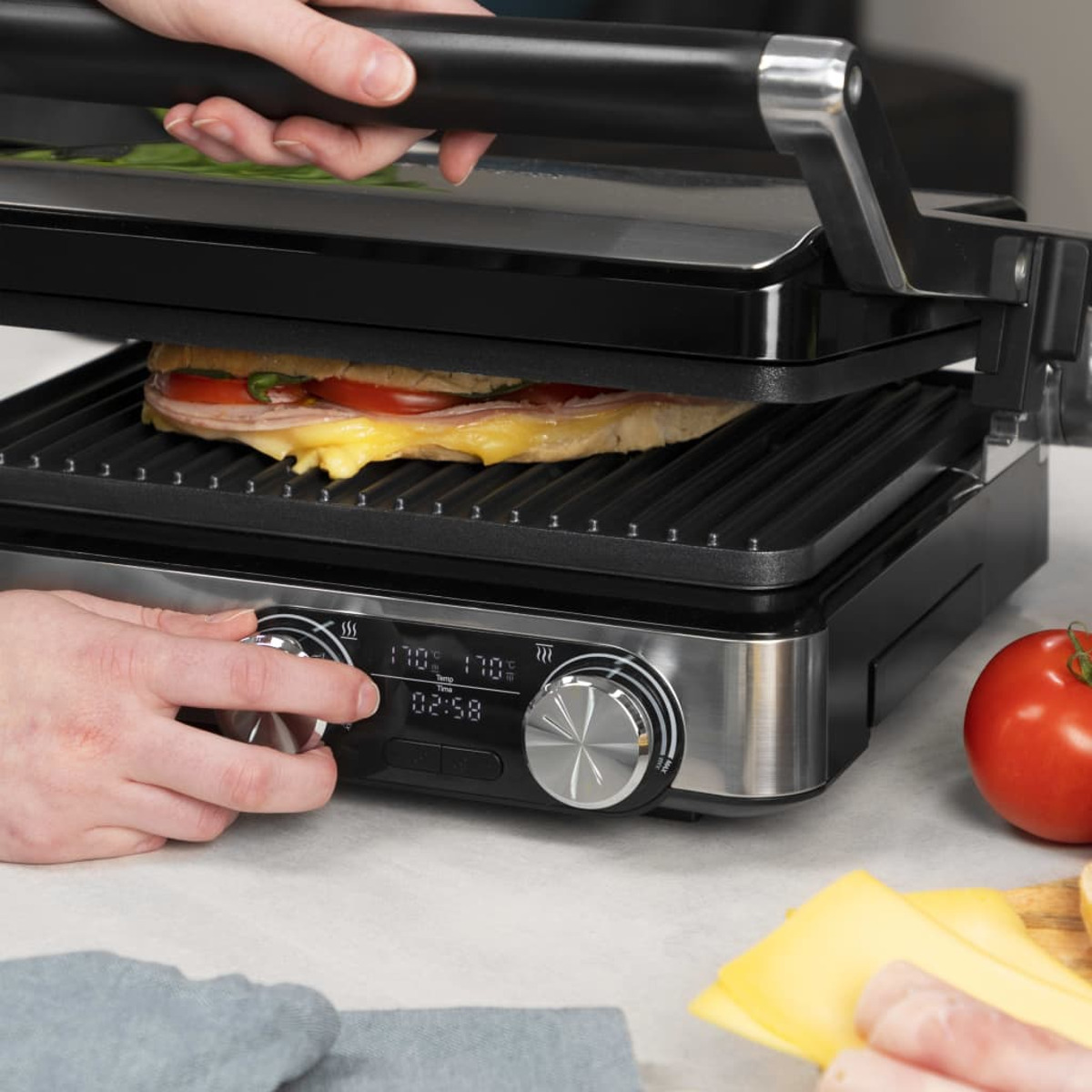 Sandwich wird auf einem schwarzen Grill gegrillt. Hände passen die Einstellungen an. Tomate und Käse sind sichtbar.