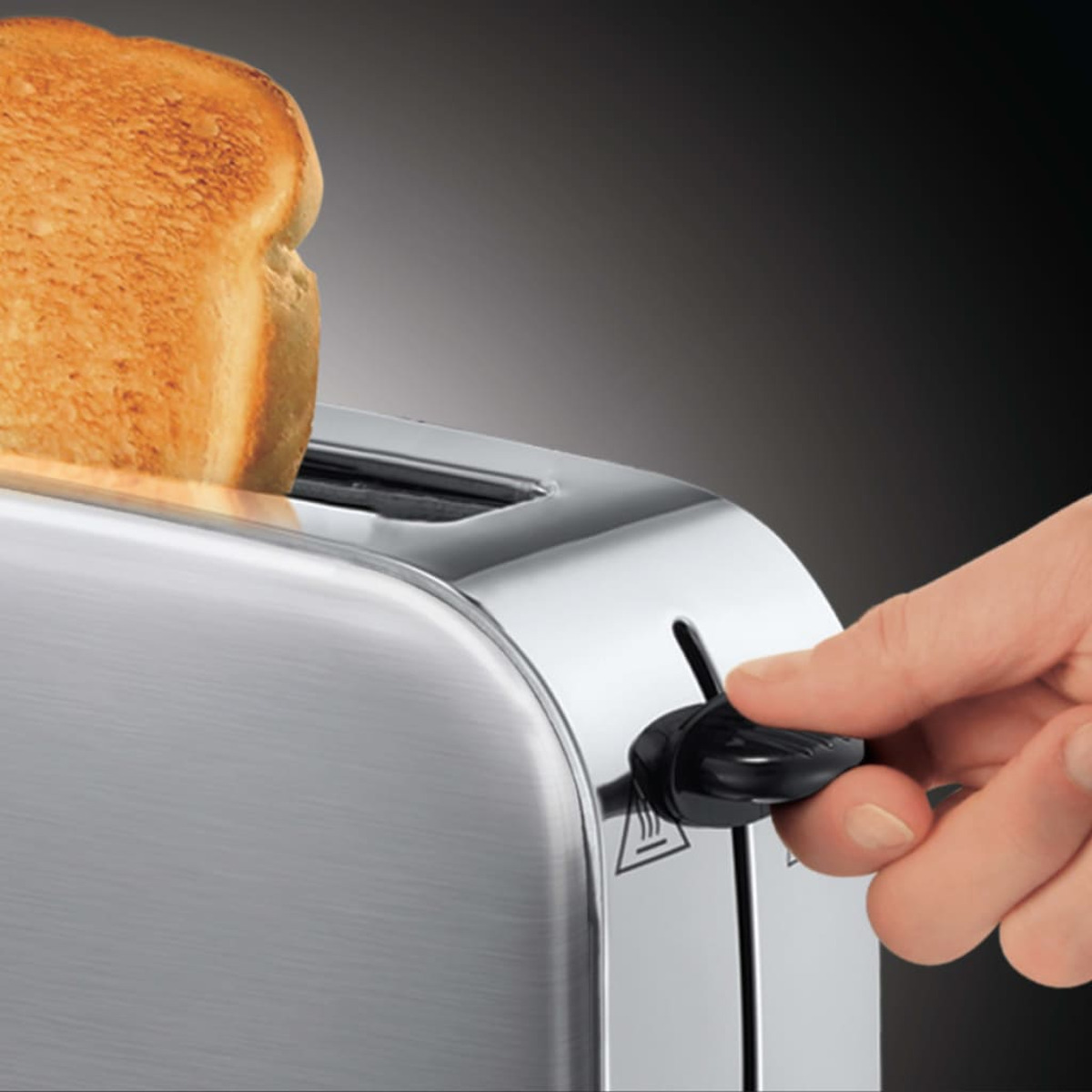 Toster ze kromką chleba opuszczaną do środka. Ręka obsługuje dźwignię.