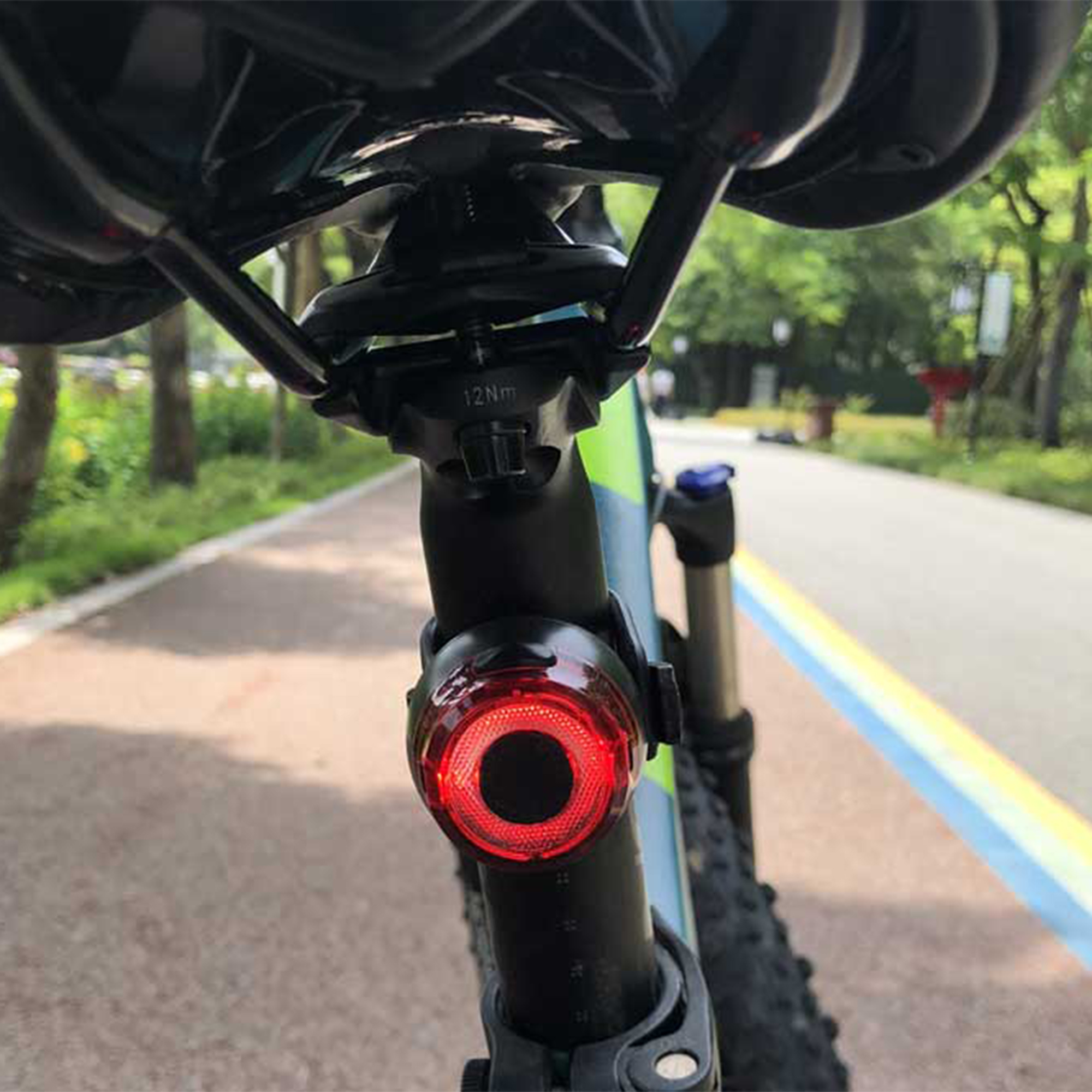 Das Heck eines Fahrrads mit rotem Rücklicht an der Sattelstütze, vor einer Straße.