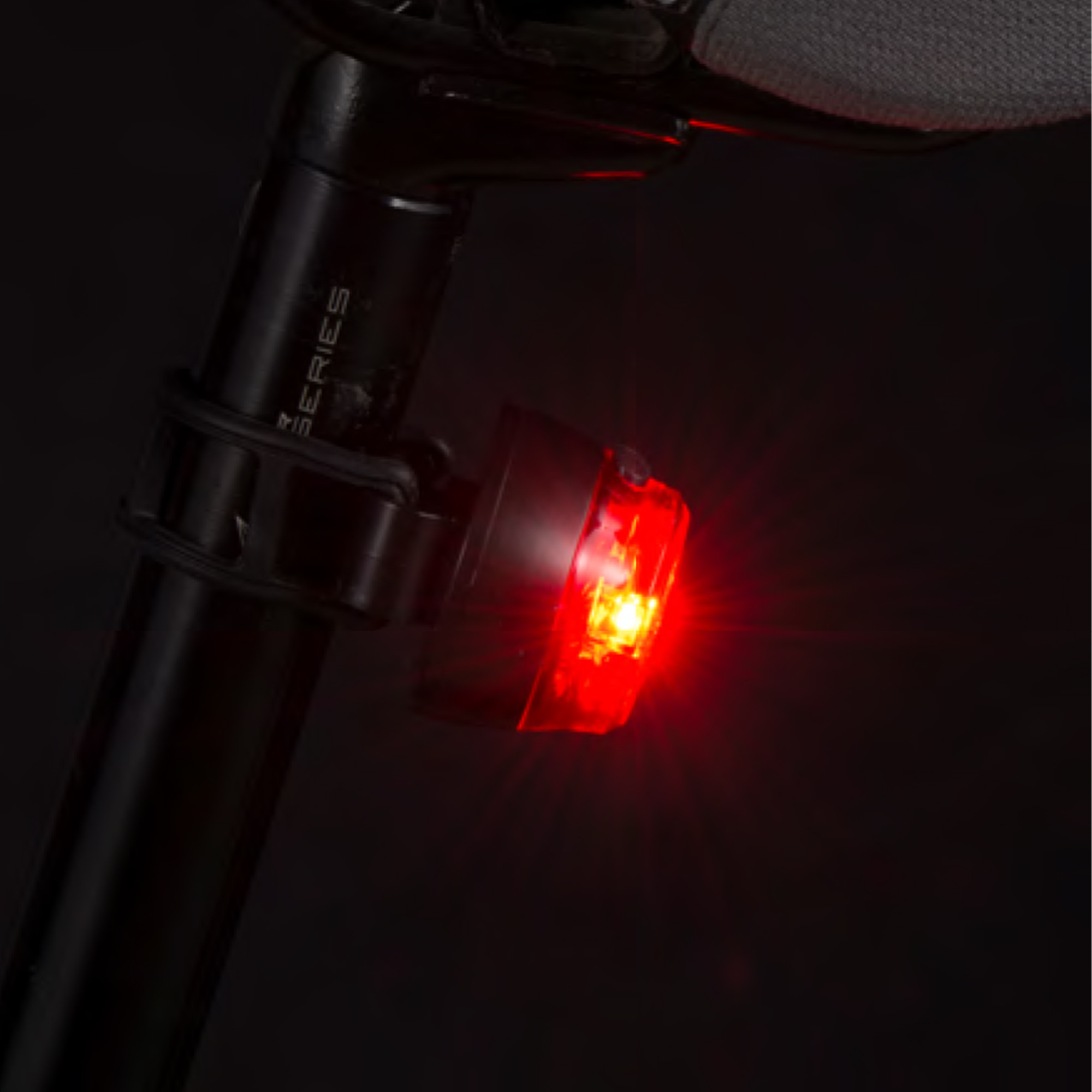 Rotes Fahrradrücklicht an einer schwarzen Sattelstütze montiert, hell leuchtend.