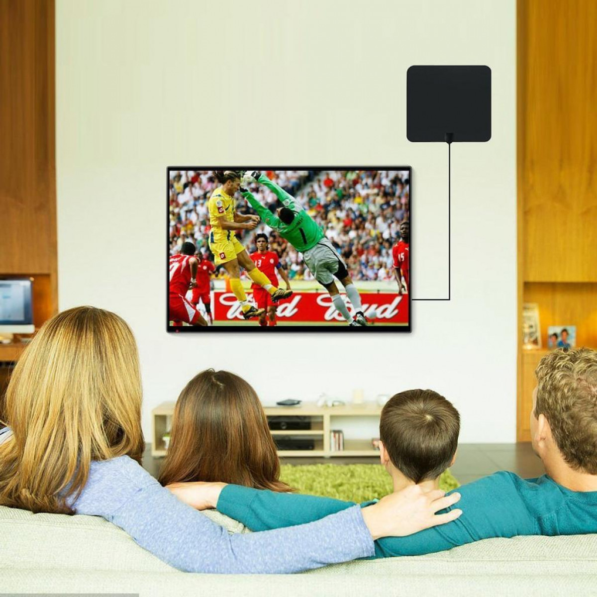 Een gezin kijkt tv. Er staat een voetbalwedstrijd op het scherm en er staat een antenne boven de tv.
