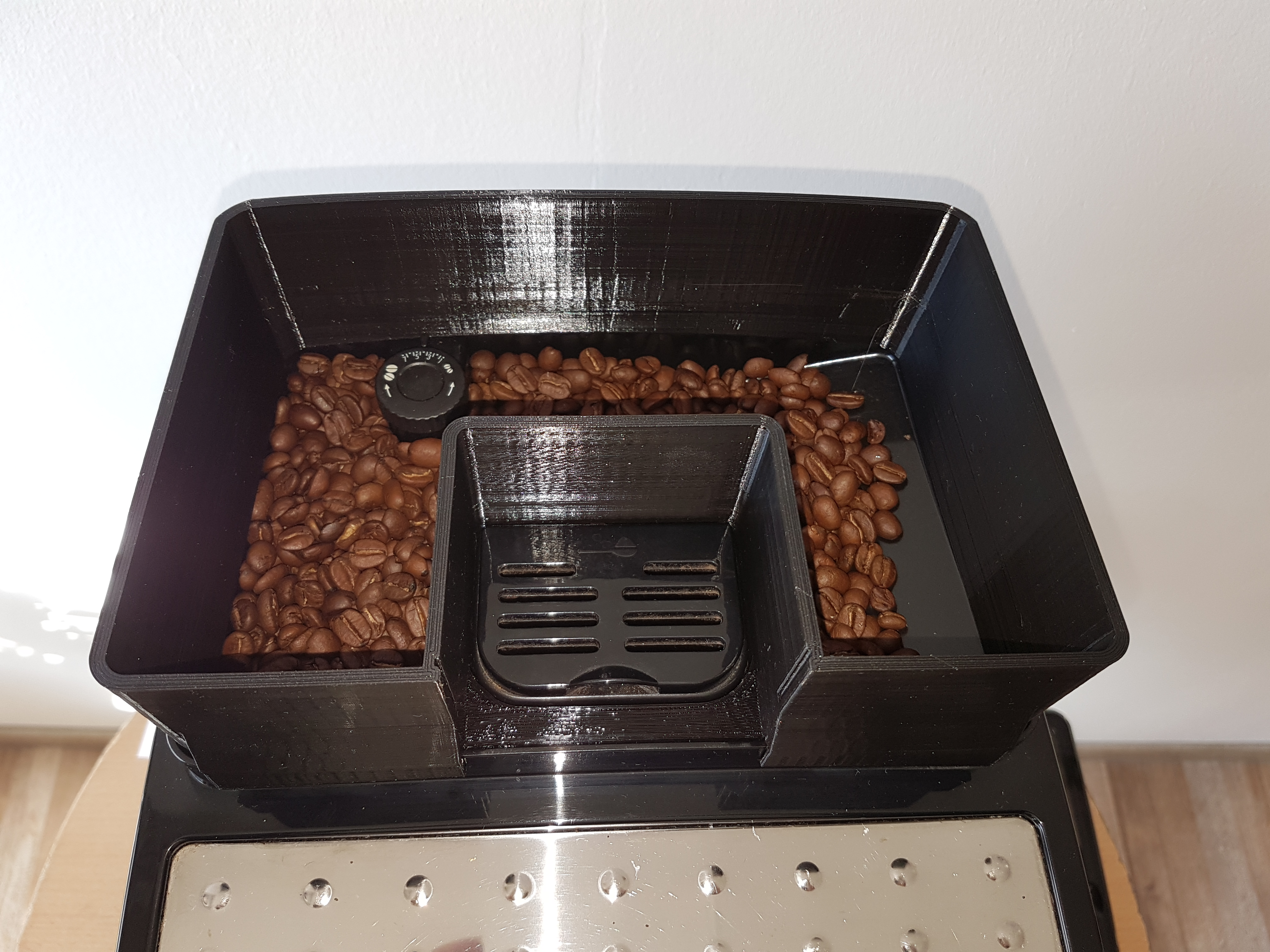 Kaffeebohnen füllen einen schwarzen Behälter mit Ausguss, von oben gesehen.