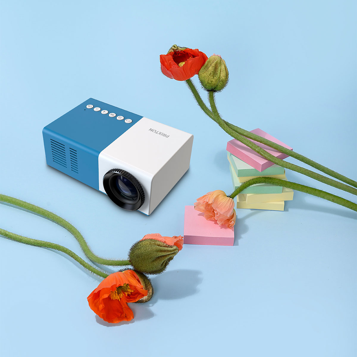 Een blauwe en witte projector met bloemen en plaknotities. Rode klaprozen en roze notities op een blauwe achtergrond.