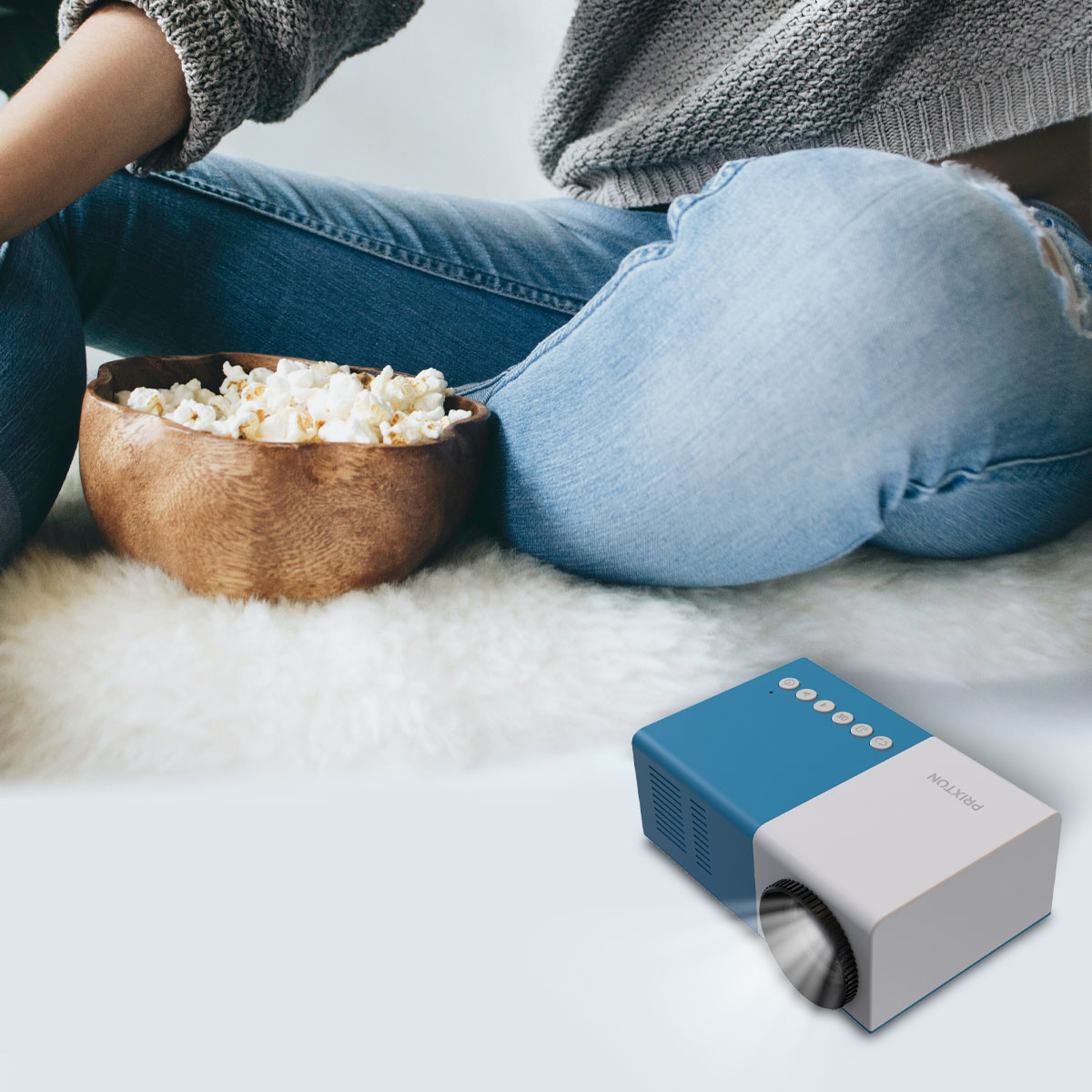Een persoon die zit met popcorn in een kom, een blauw-witte projector op de vloer.