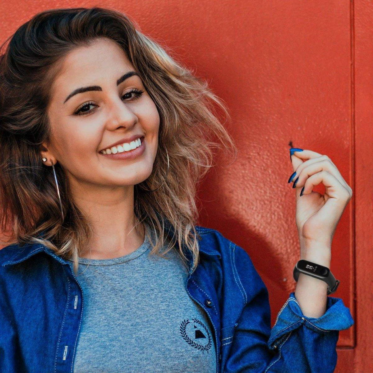 Frau mit Jeansjacke und Smartband am Handgelenk lächelt in die Kamera.