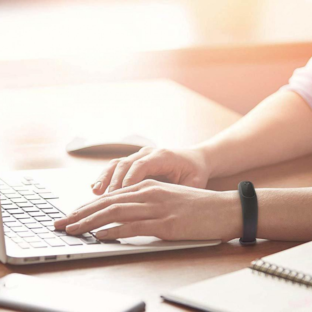 Person benutzt Laptop mit schwarzem Fitness-Tracker-Armband am Handgelenk.