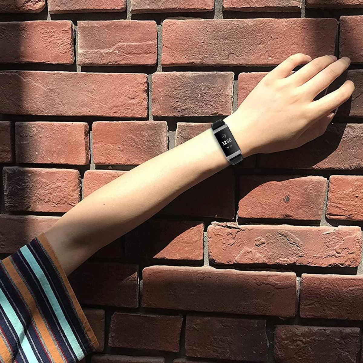 Der Arm einer Person, die eine schwarze Smartwatch trägt, deren Display die Uhrzeit anzeigt.