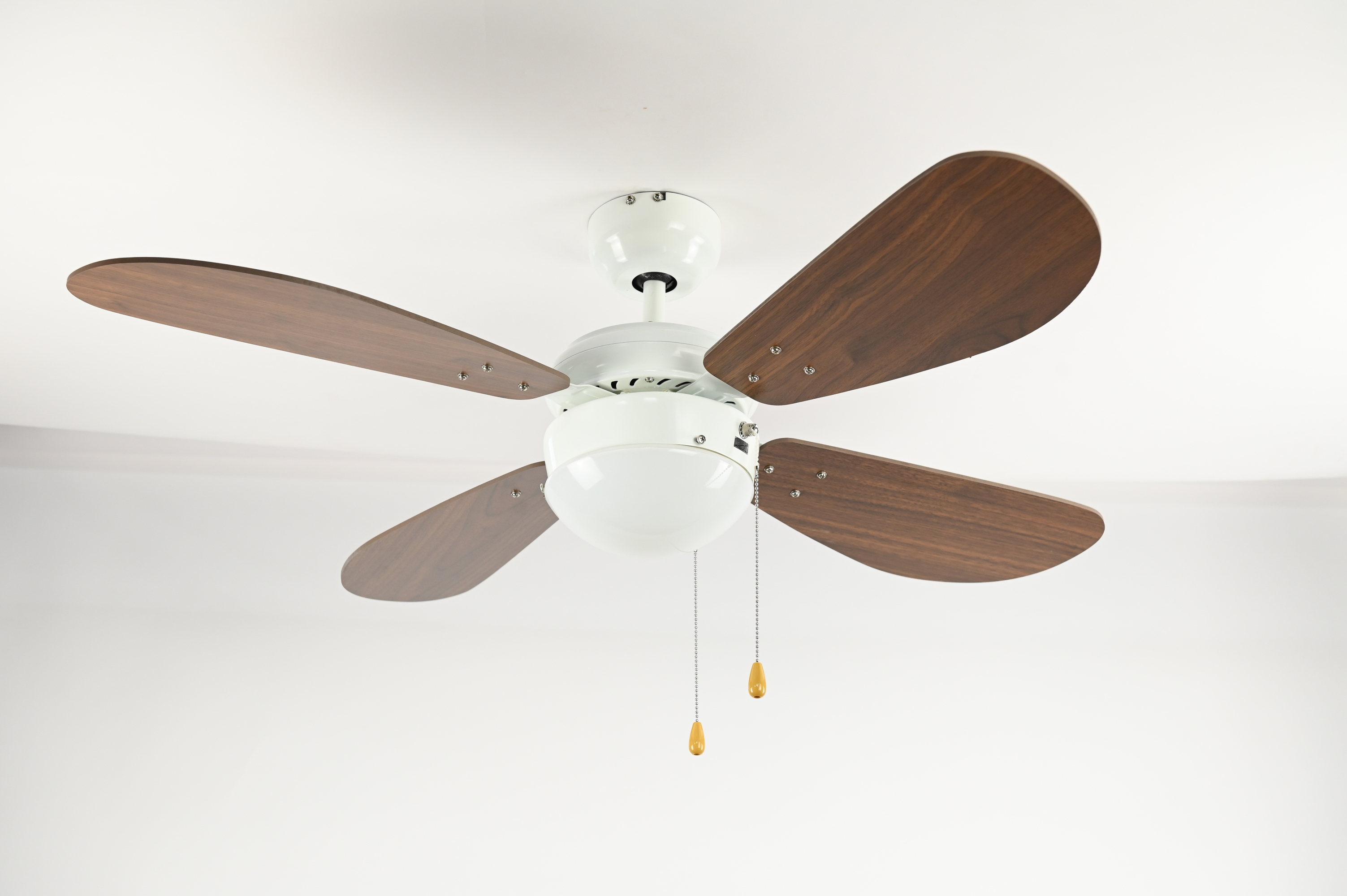 Weißer Deckenventilator mit braunen Flügeln. Er hat ein Licht und zwei Zugketten darunter.
