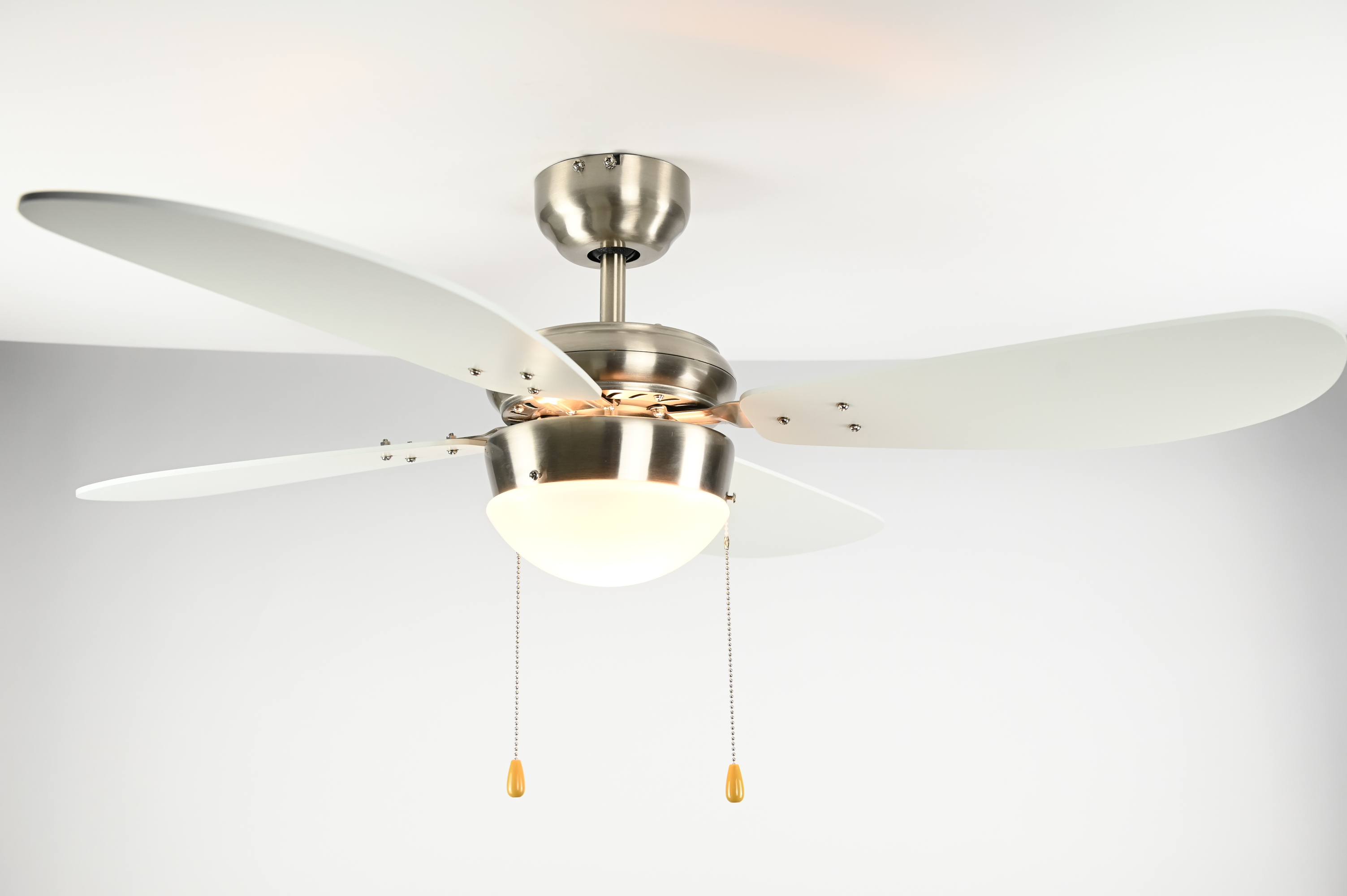 Eine Deckenventilator mit vier weißen Flügeln, einer Leuchte und herabhängenden Zugketten.