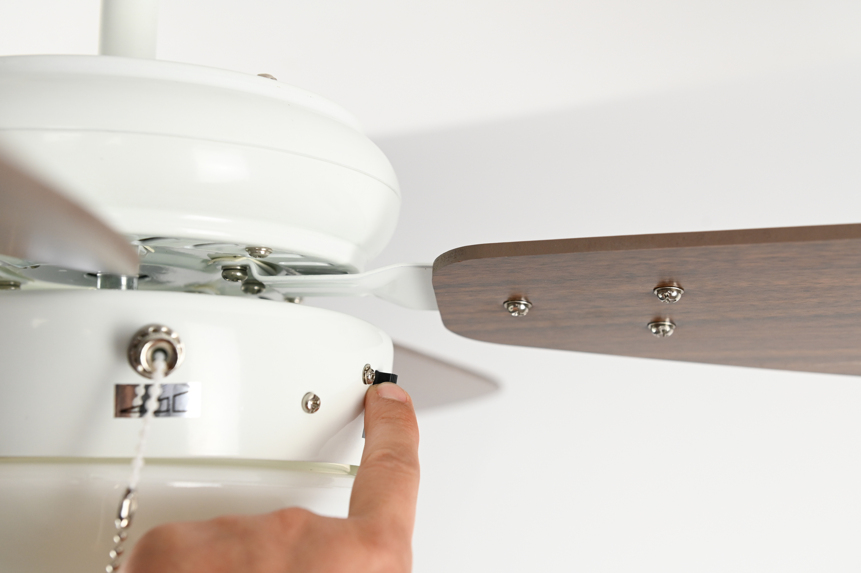 Eine Hand schaltet einen Deckenventilator ein, Nahaufnahme vor weißem Hintergrund.