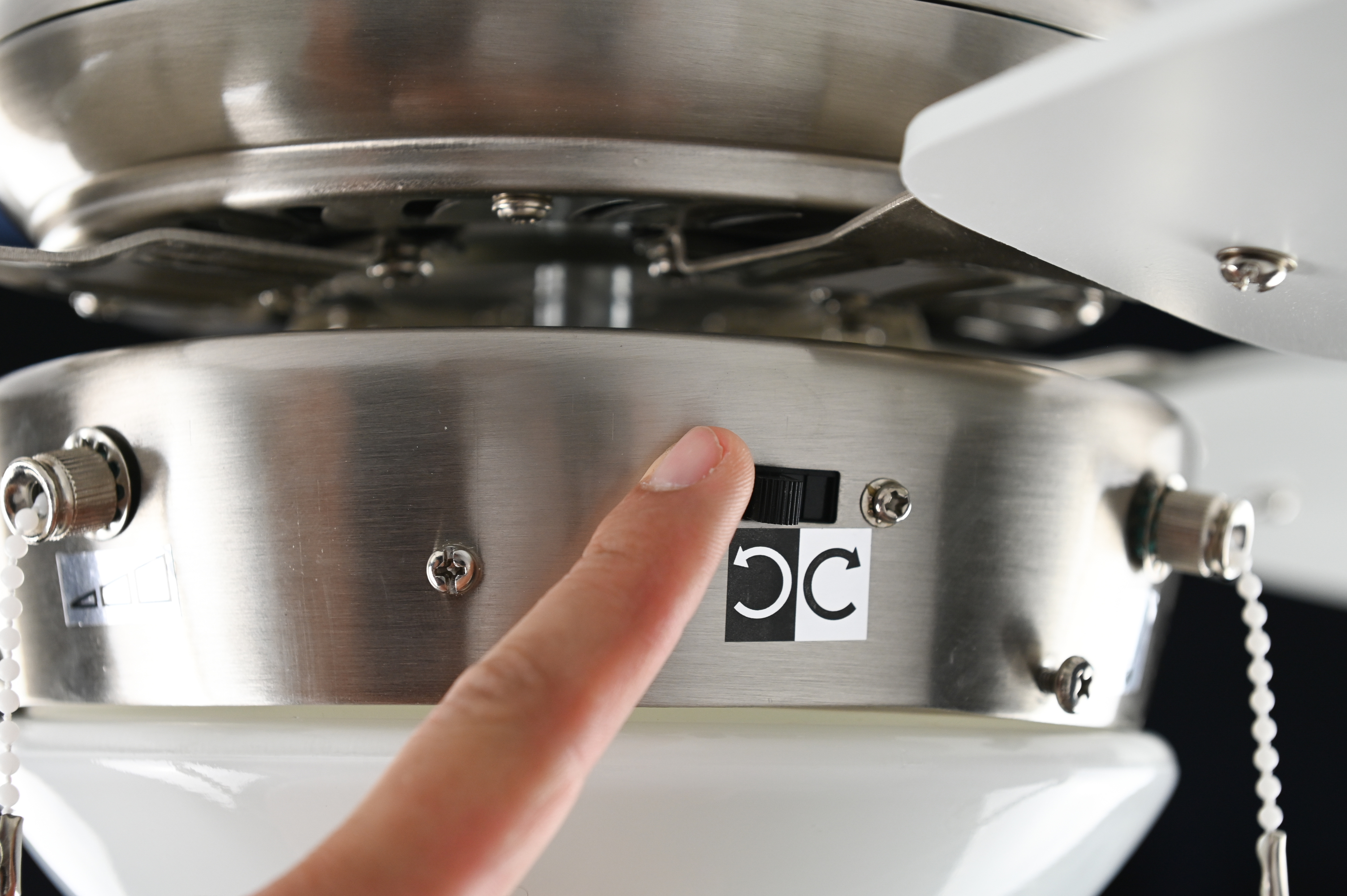 Eine Hand, die einen Schalter an einem Deckenventilator mit kreisförmigen Pfeilen drückt.