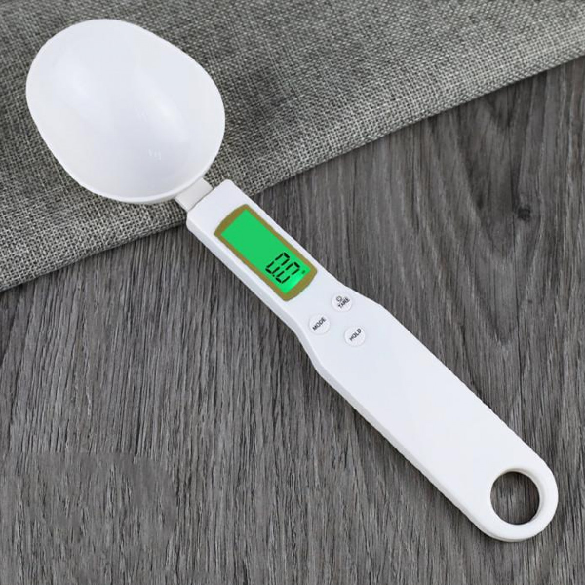 Biała cyfrowa waga łyżkowa z zielonym wyświetlaczem. Łyżka znajduje się na drewnianej powierzchni.