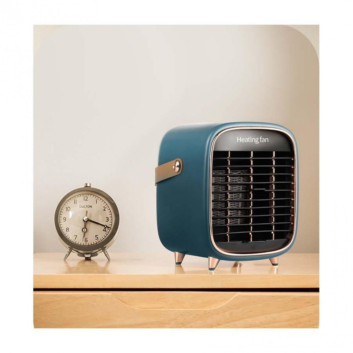 Turkusowy wentylator grzewczy na drewnianym stole, z zegarem. Wentylator ma złoty uchwyt. Białe tło.