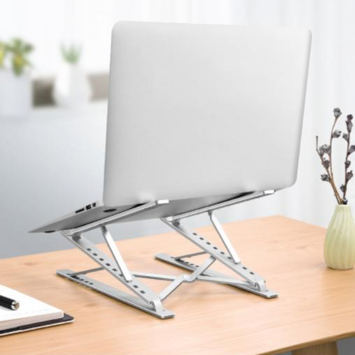 Laptop auf einem silbernen Laptopständer. Holztisch und Vase im Hintergrund.