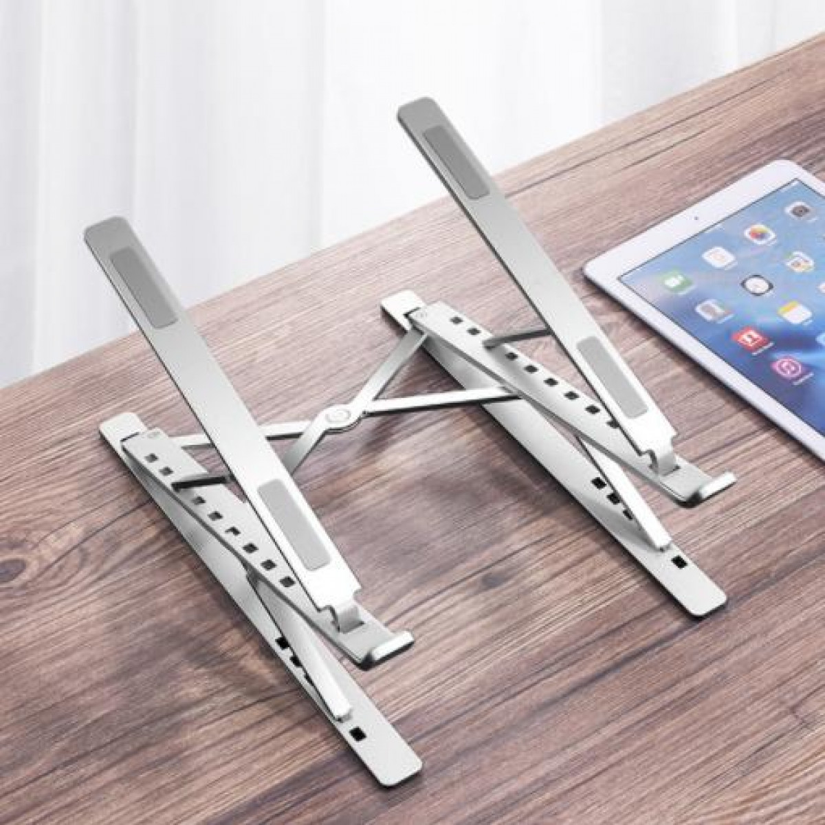 Silberner Laptop-Ständer. Der Ständer hält ein Tablet auf einem Holztisch.