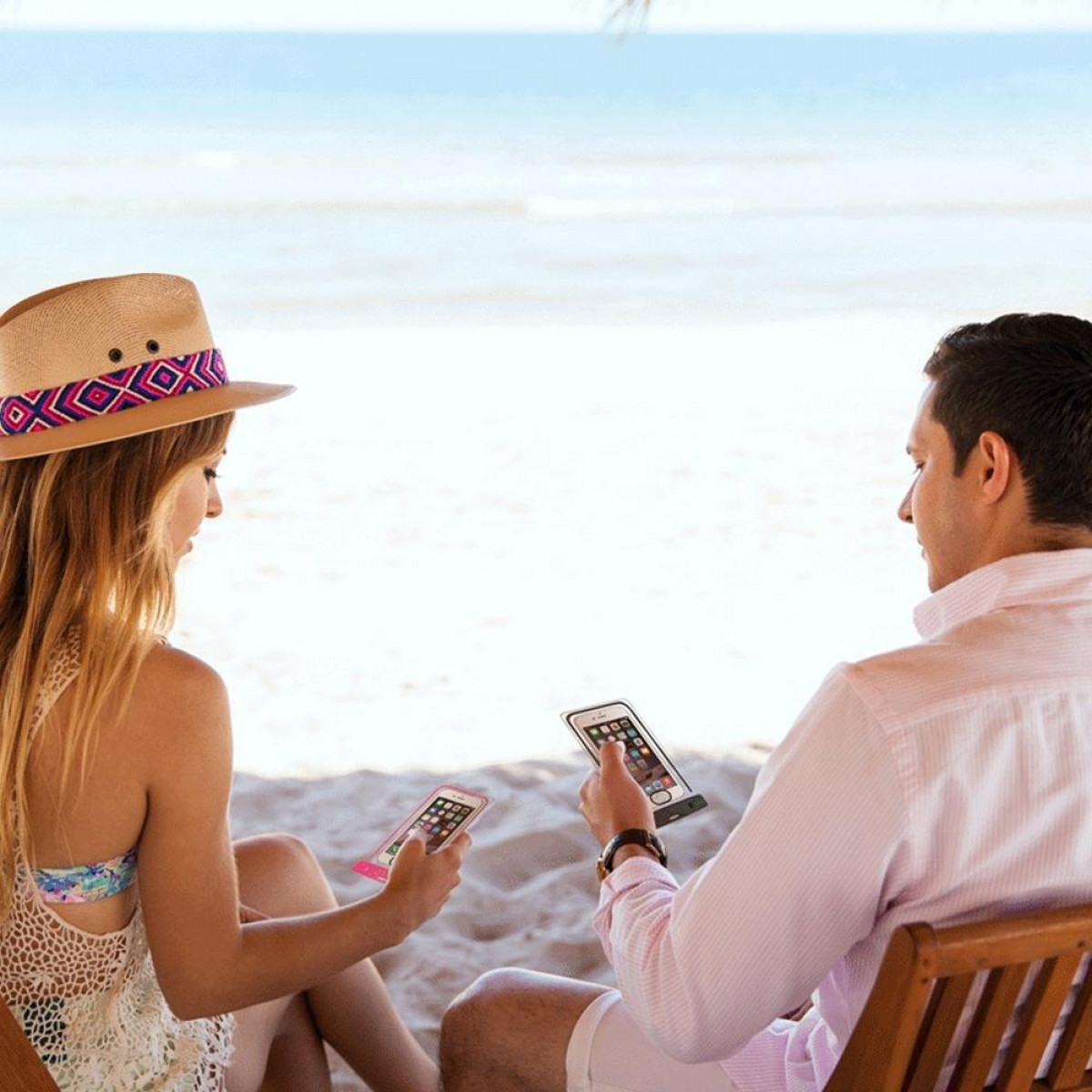 Dwie osoby na plaży, każda trzyma smartfon. W tle plaża i ocean.