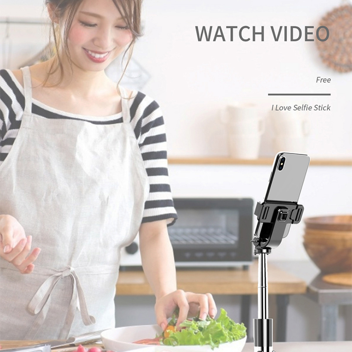 Kobieta gotuje w kuchni, trzymając miskę sałatki, z telefonem na patyku do selfie do oglądania filmów.