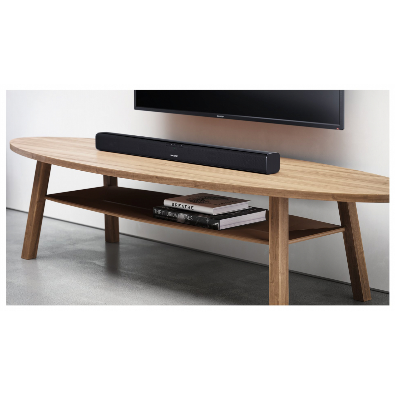 Drewniany stół z czarnym soundbarem i książkami. Telewizor na ścianie w tle.