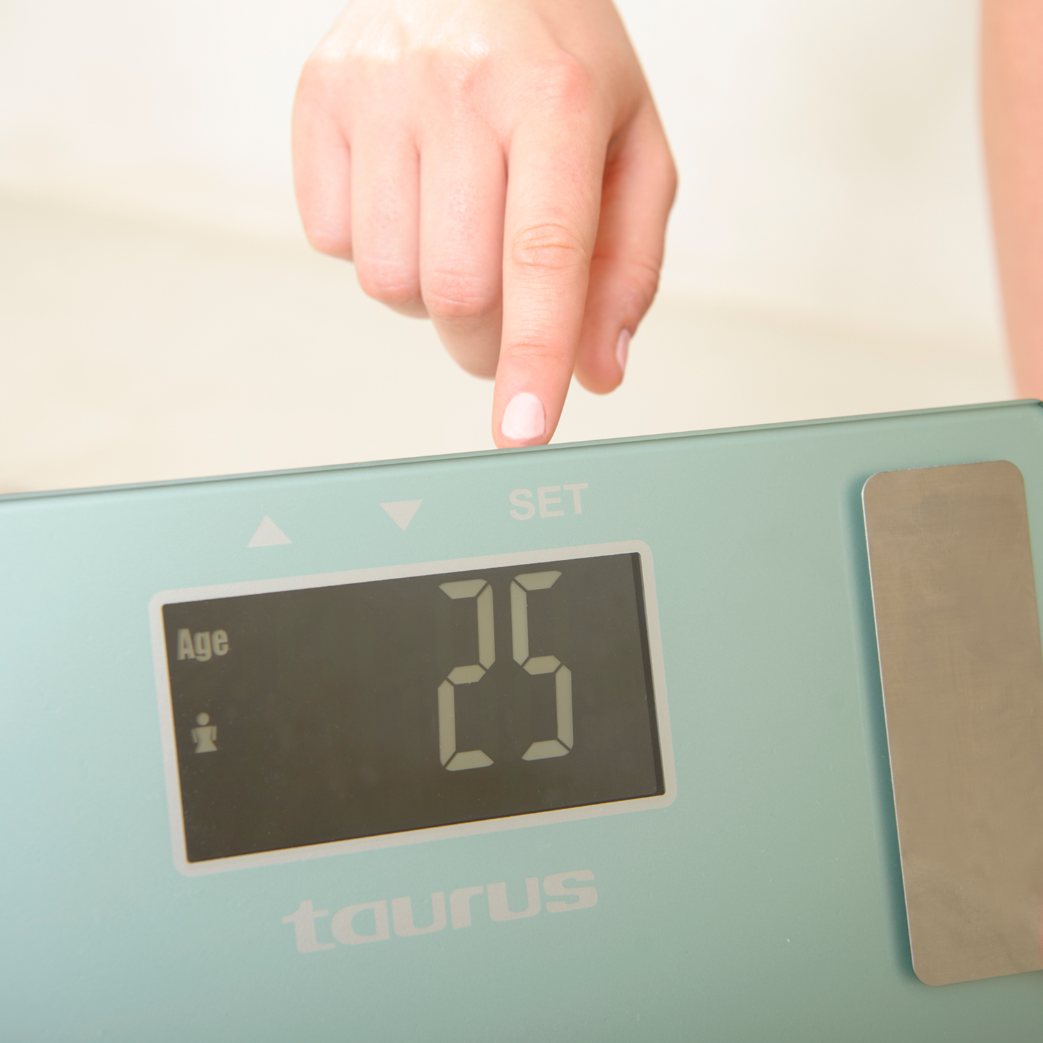 Ręka dotykająca wagi cyfrowej wyświetlającej liczbę 25 i słowo 'Taurus'.