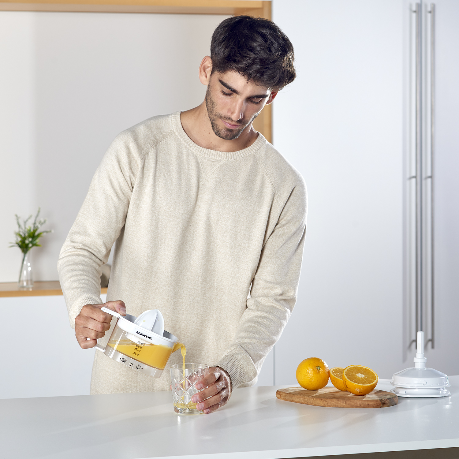 Mężczyzna wyciska pomarańcze do szklanki za pomocą wyciskarki. Pomarańcze i części wyciskarki na stole.