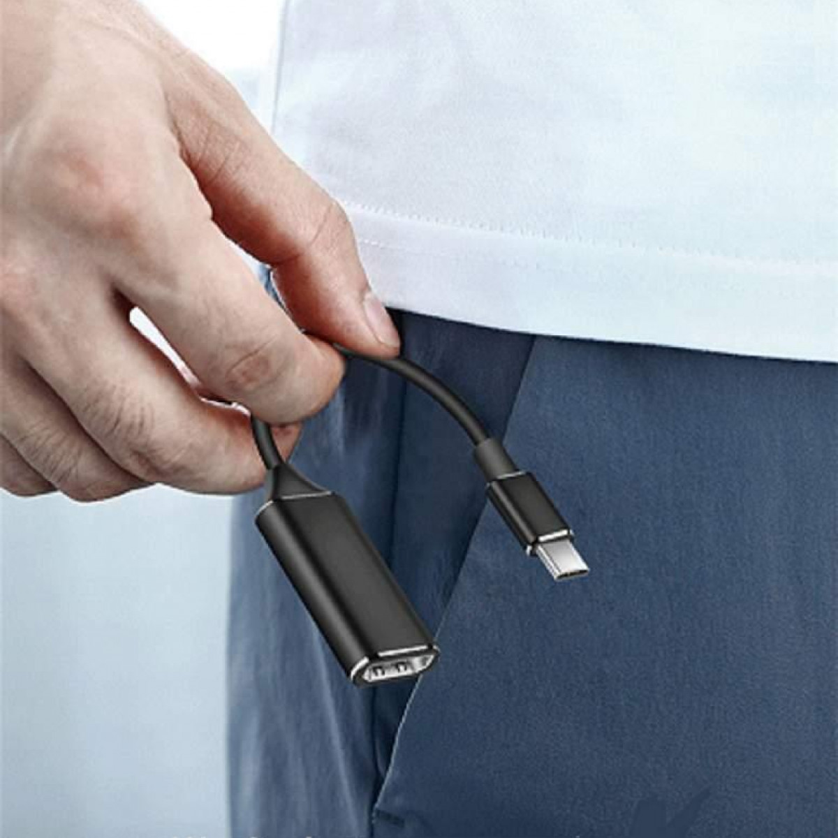 Osoba trzymająca czarny kabel adaptera USB-C do HDMI, tłem są jej spodnie.