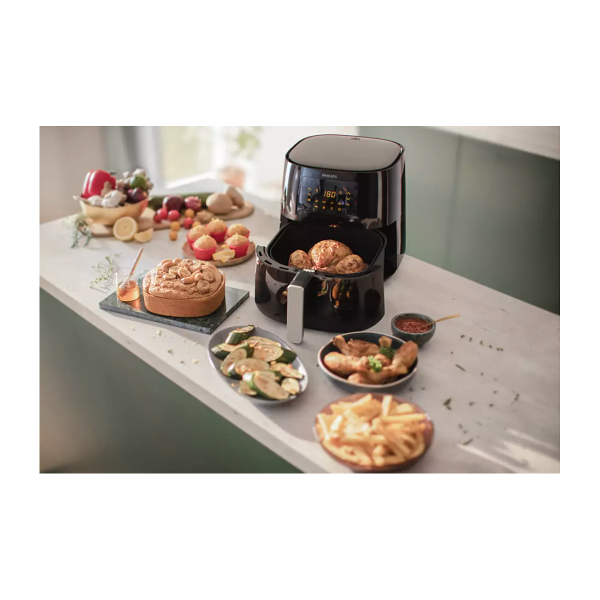Airfryer en eten op een wit oppervlak: kip, cake, friet en groenten.