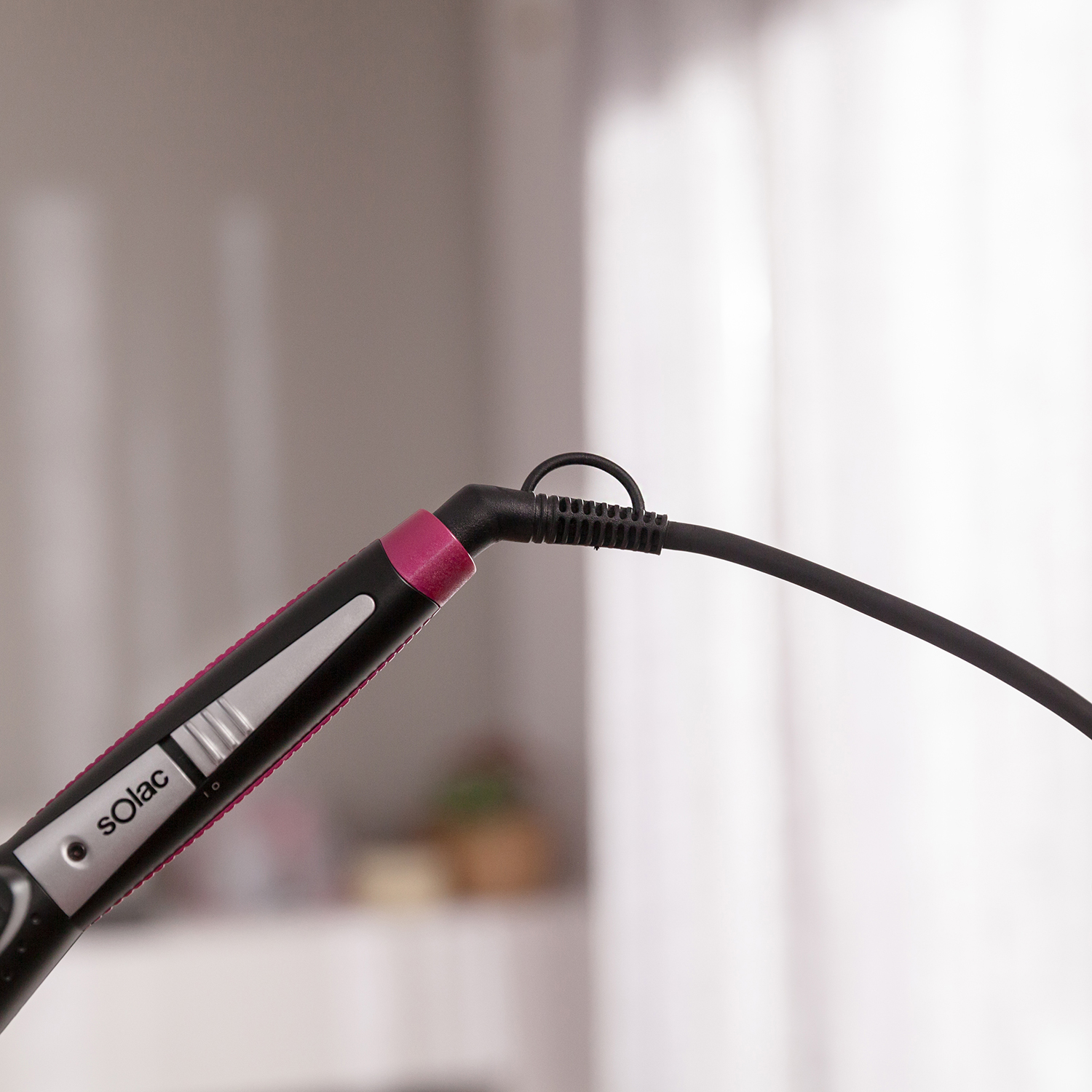 Plancha para el pelo con cable negro y detalle rosa.