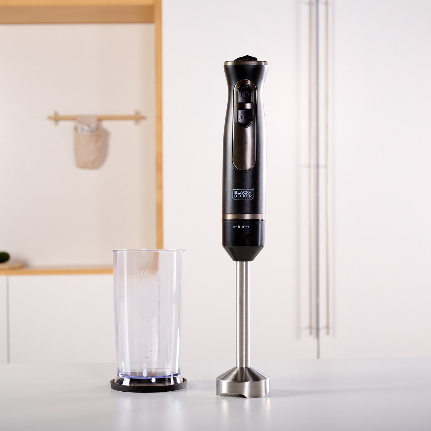 Czarny i srebrny blender ręczny z przezroczystym kubkiem miarowym na białej powierzchni.