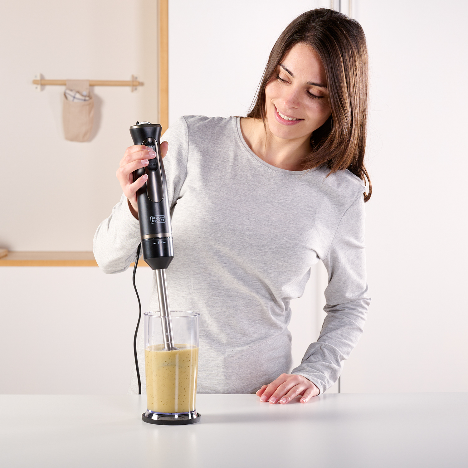 Kobieta używa blendera w kuchni, z szklanką zielonego płynu.