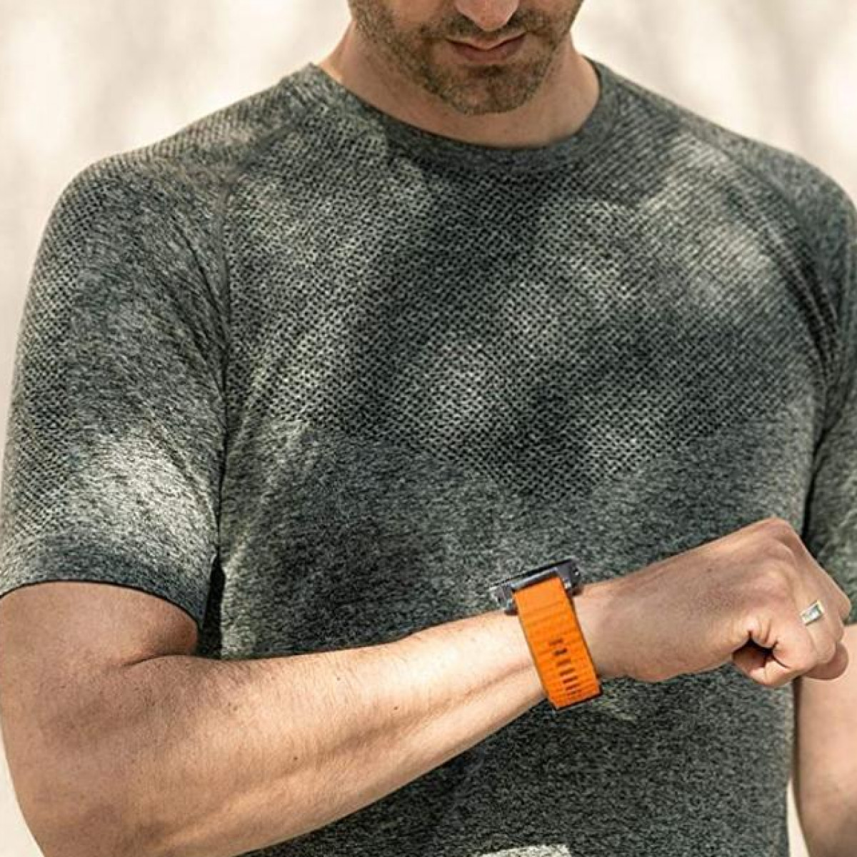 Mężczyzna w szarej koszulce, patrzący na pomarańczowy smartwatch na nadgarstku.