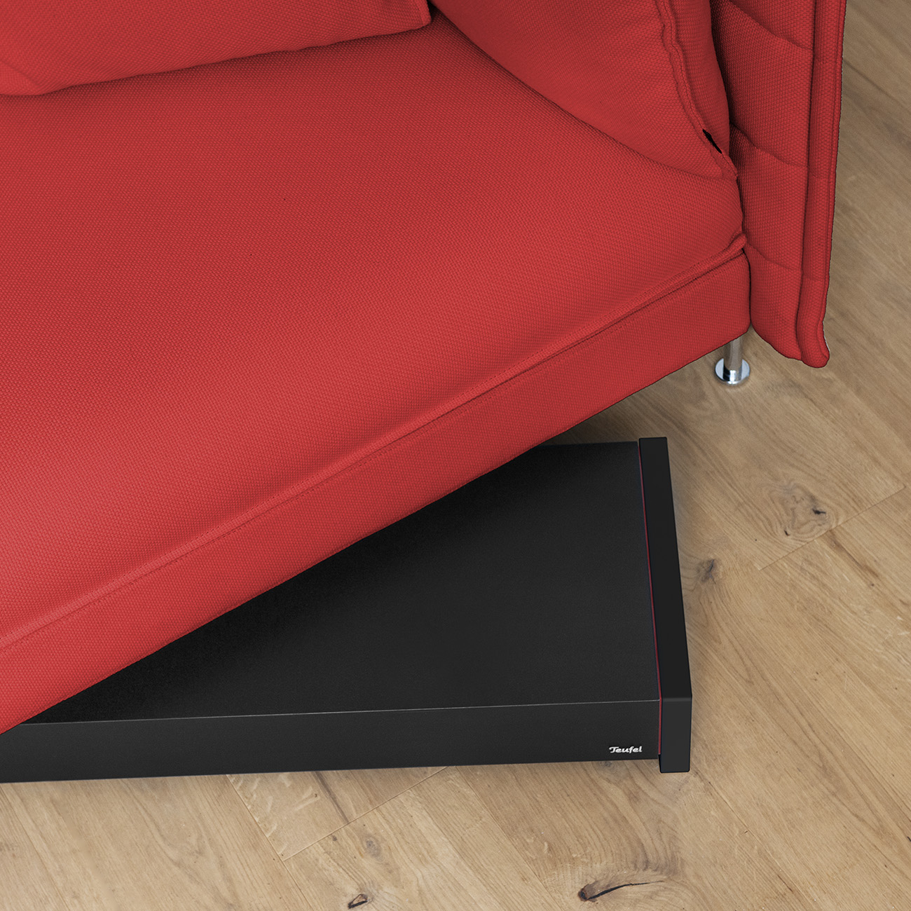 Rotes Sofa mit schwarzem Sockel und Teufel-Soundsystem auf Holzboden.