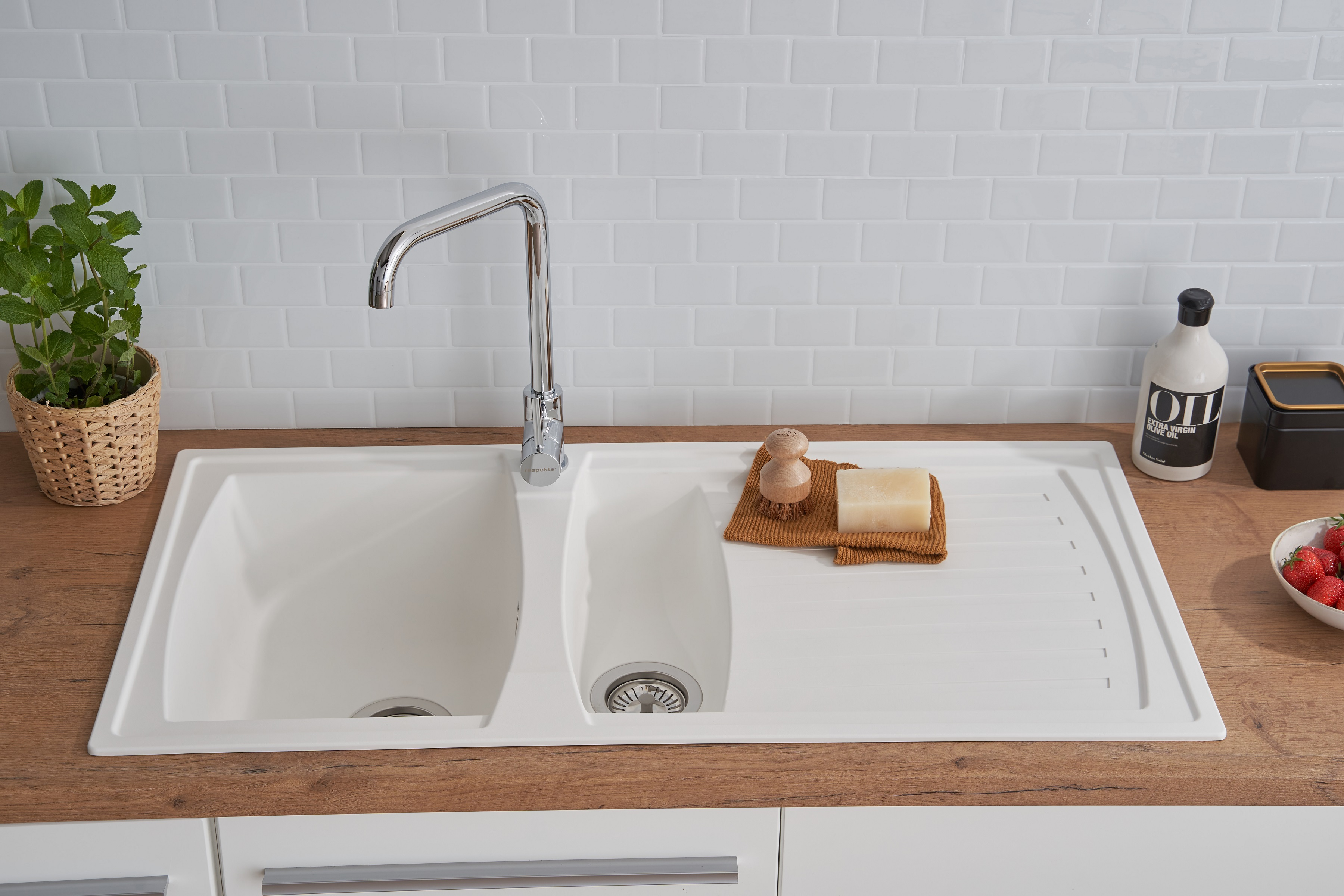 Weißes Küchenbecken mit zwei Becken, Wasserhahn und Holz-Arbeitsplatte. Seife, Bürsten und Erdbeeren.