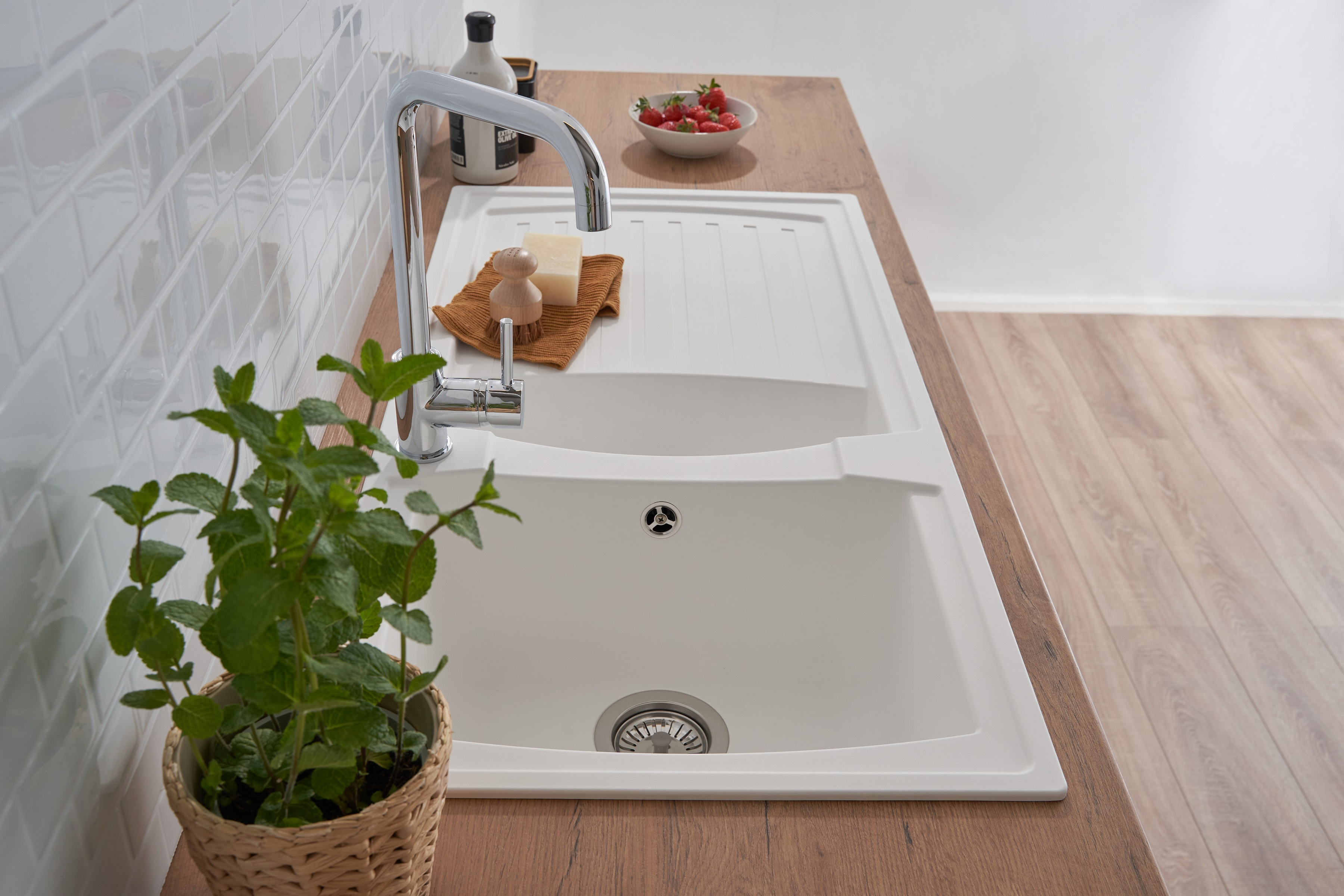 Küchenspüle mit Wasserhahn, Seife und Pflanze. Erdbeeren auf einer Holz-Arbeitsplatte.