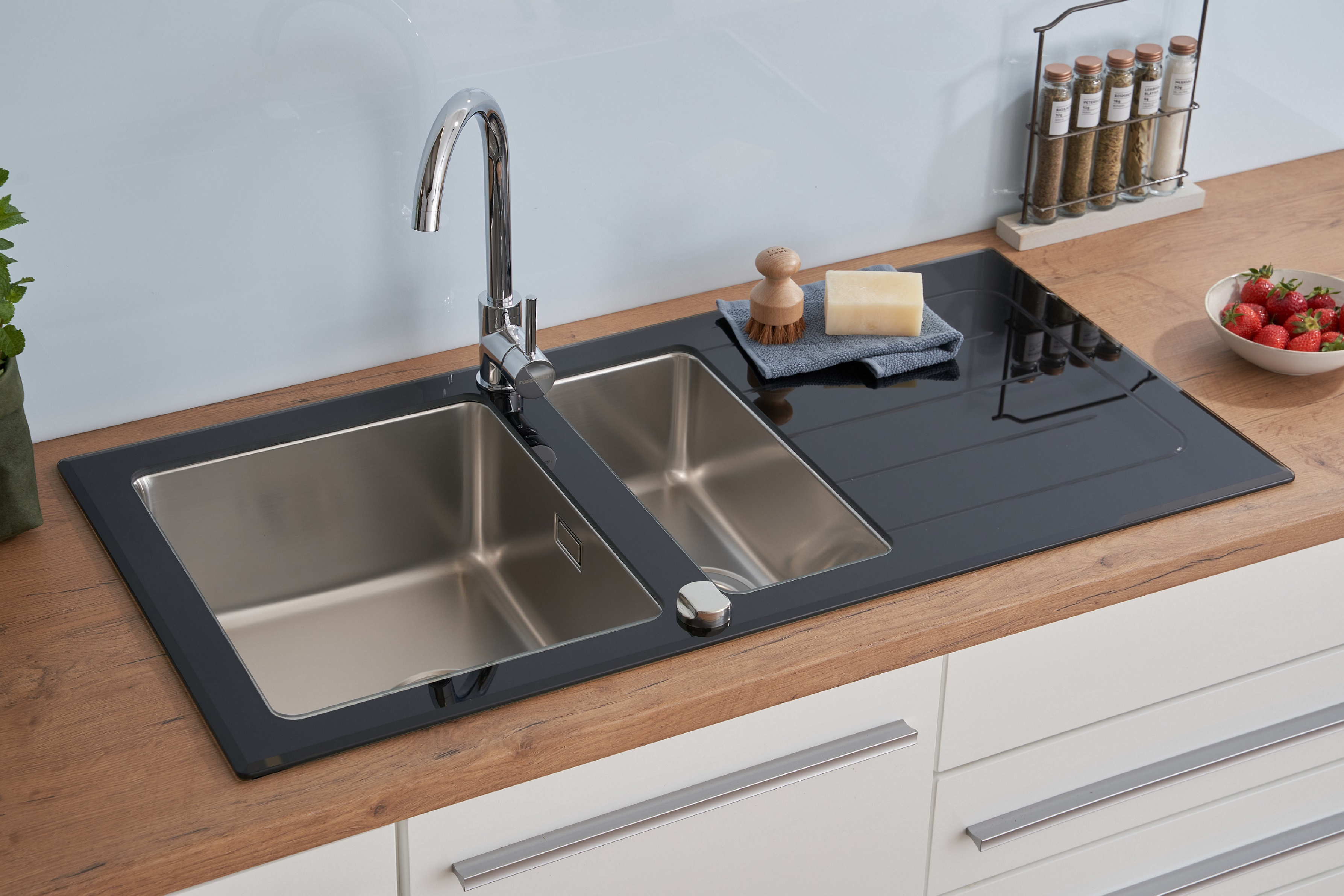 Edelstahl-Küchenspüle mit zwei Becken. Darüber ein Wasserhahn. Eine Spülbürste und Seife liegen daneben.