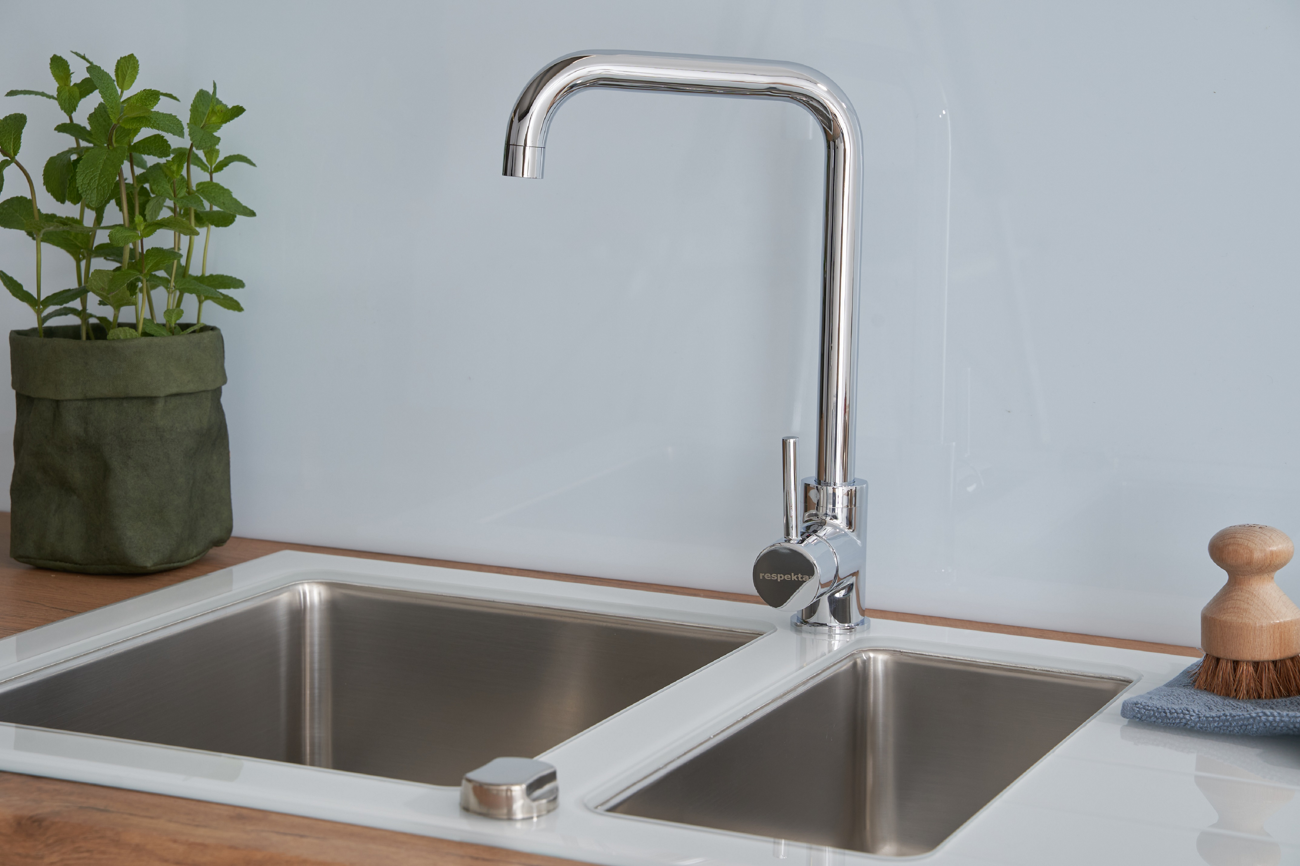 Ein Küchenbecken mit Wasserhahn und einer Pflanze. Minzepflanze in einem grünen Beutel.