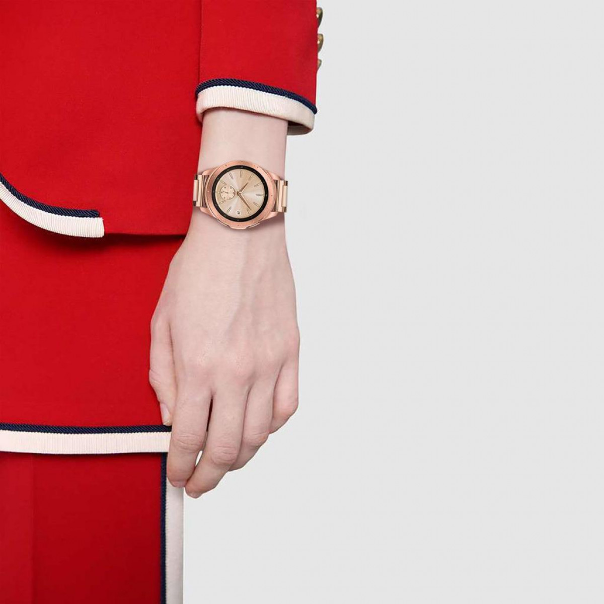 Roségoldene Uhr am Handgelenk, Person trägt roten Anzug. Weißer Hintergrund.