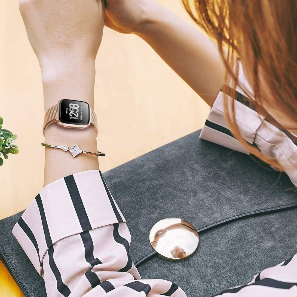 Das Handgelenk einer Frau mit Smartwatch und Armband, Tasche im Hintergrund.