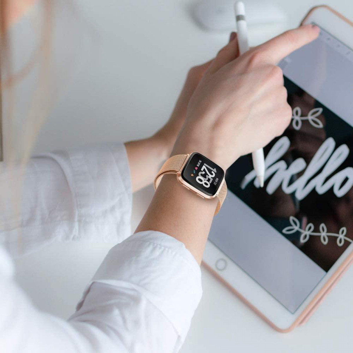 Handgelenk mit Uhr, mit weißem Tisch und Tablet im Hintergrund.