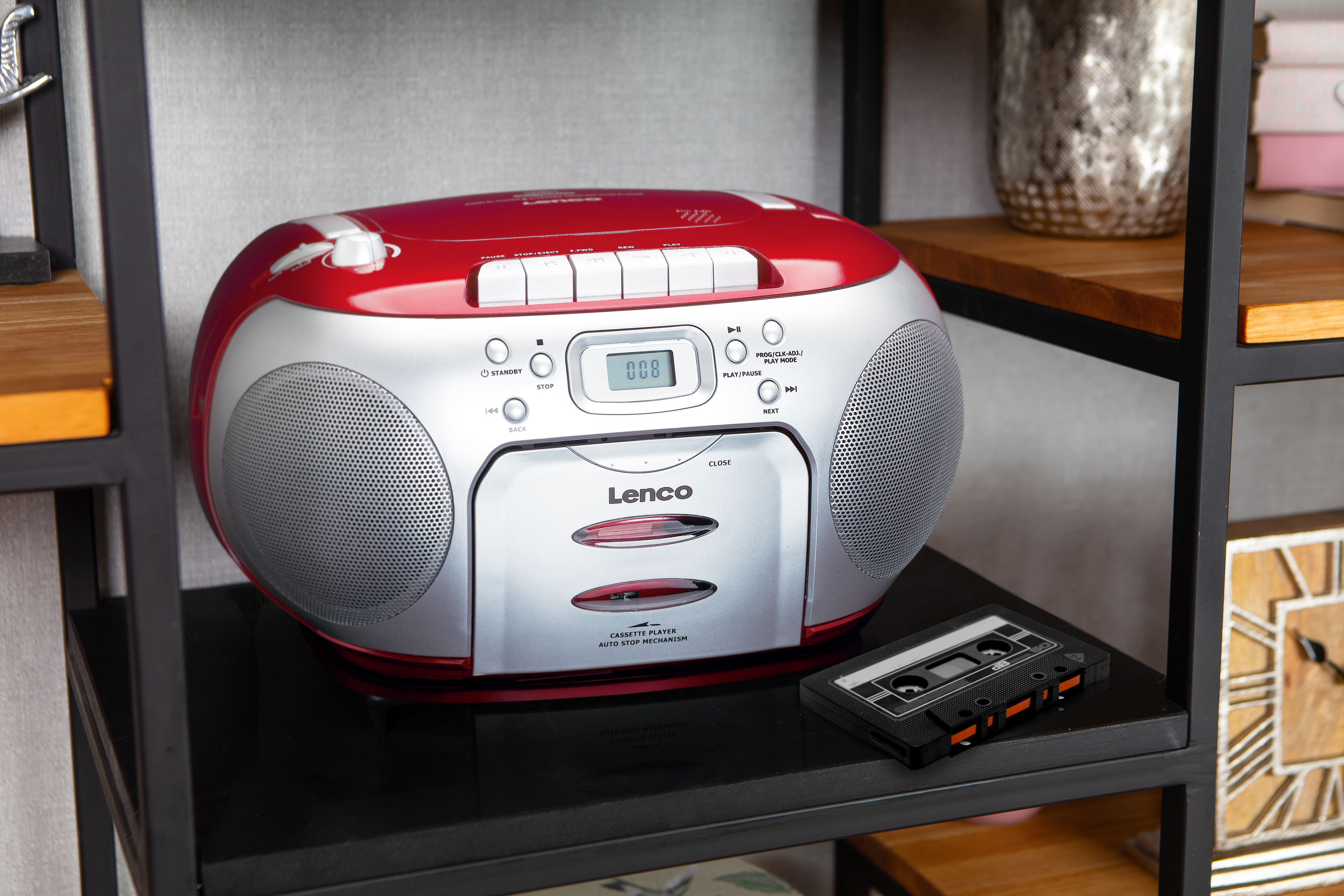 Un lecteur de cassettes Lenco rouge et argenté sur une étagère, avec une cassette à côté.