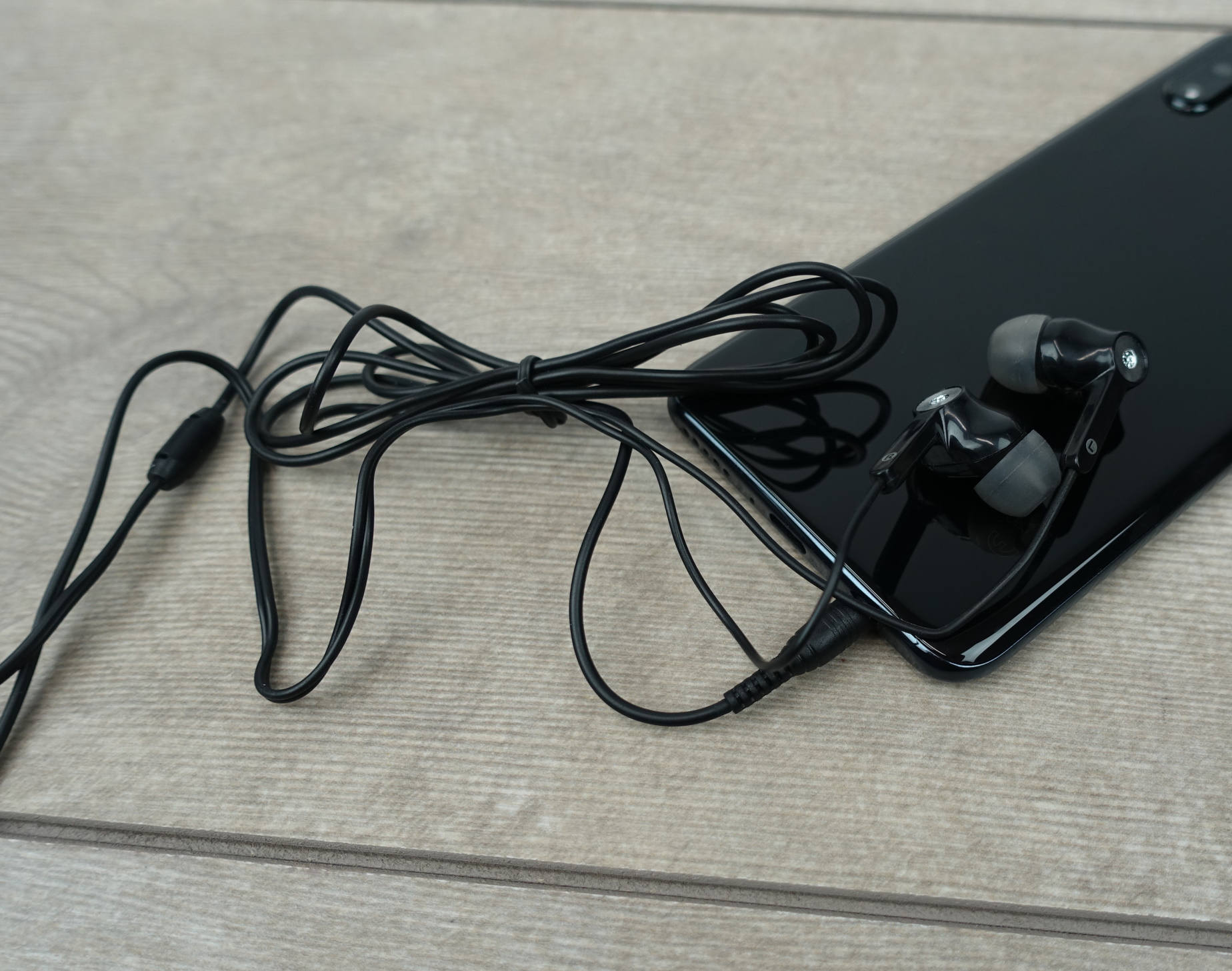 Schwarzes Telefon mit schwarzen kabelgebundenen Ohrhörern. Telefon und Ohrhörer liegen auf Holzmaserung.