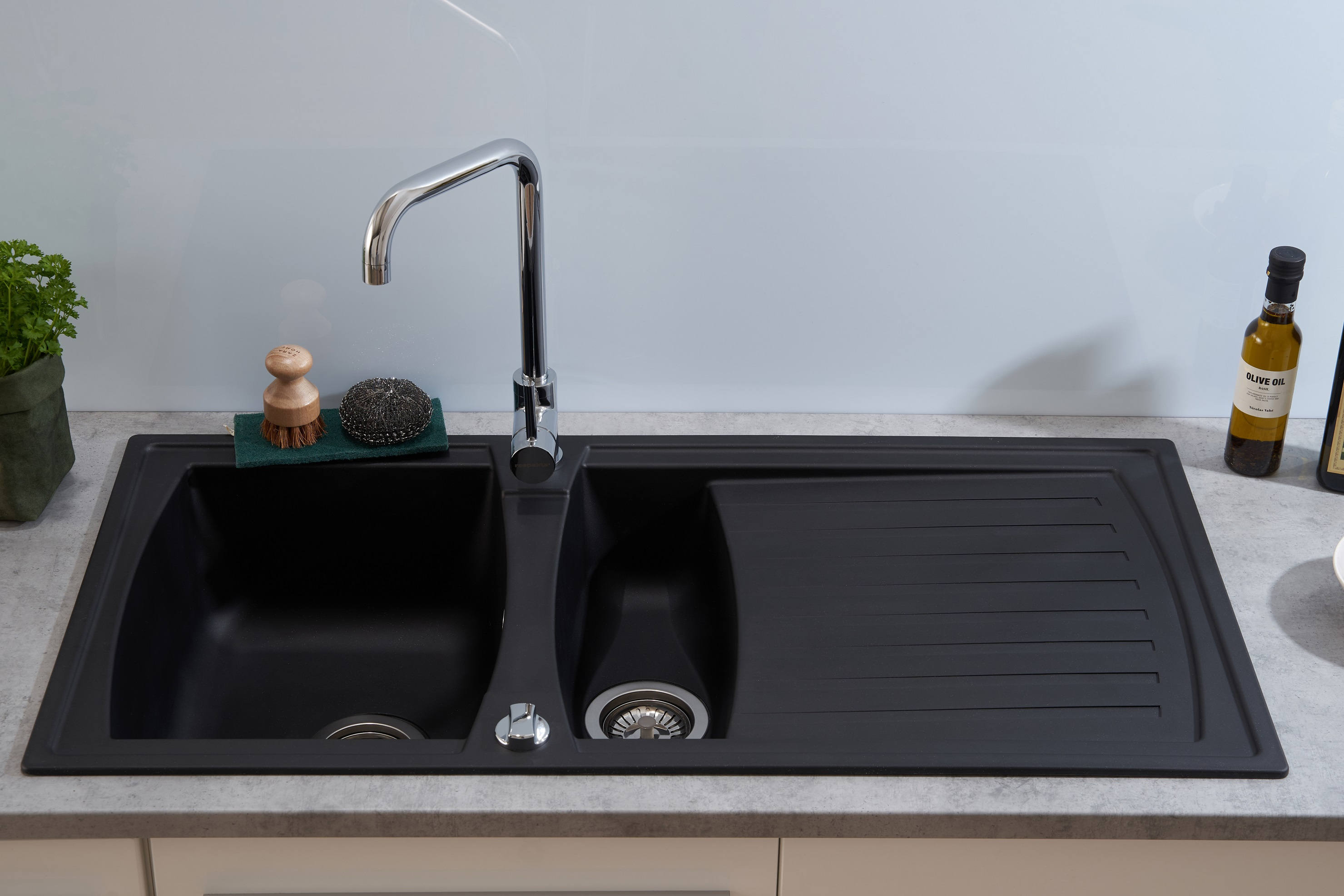 Schwarzes Küchenbecken mit zwei Becken und Wasserhahn. Der Hintergrund ist hellblau.