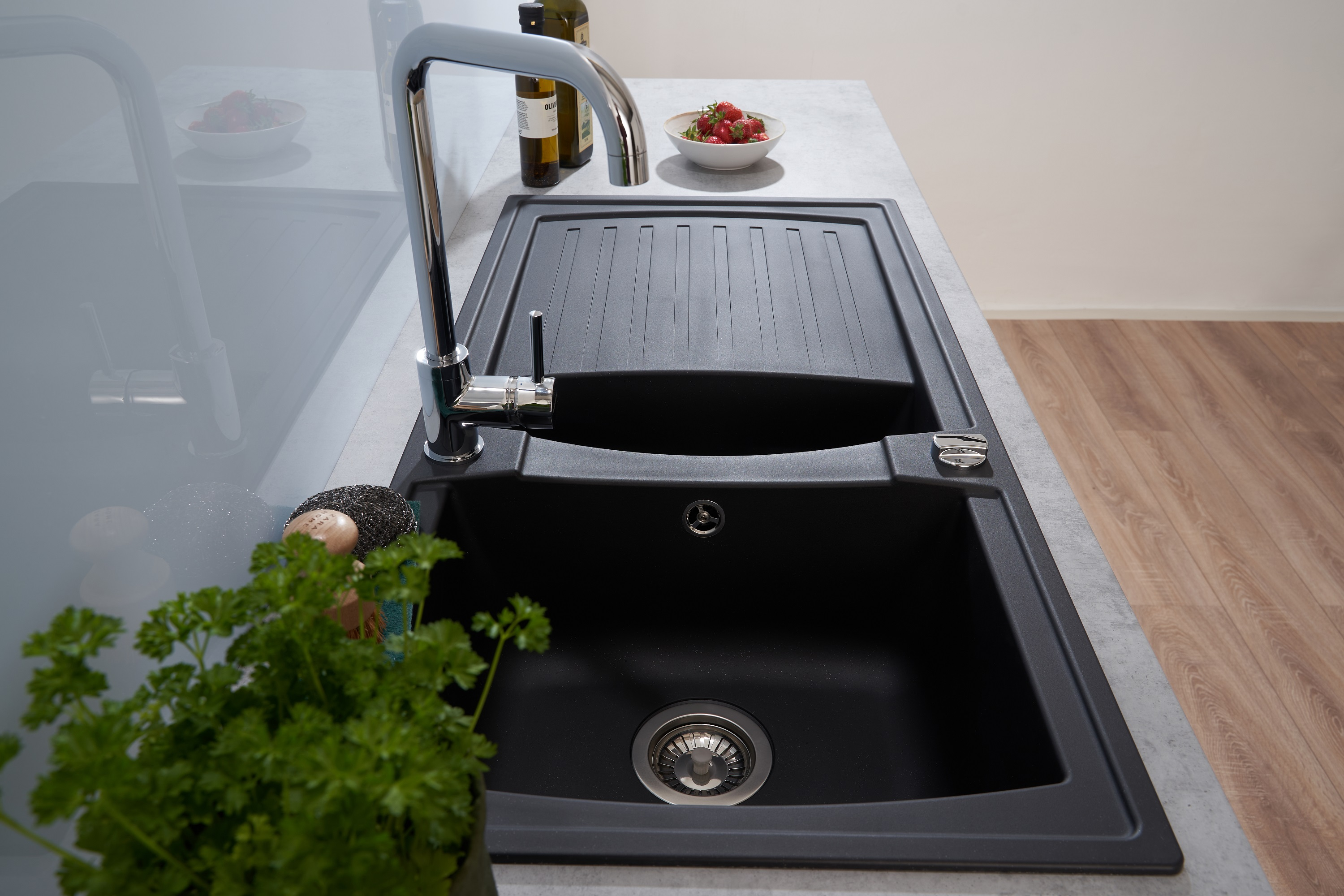 Ein schwarzes Küchenbecken mit Wasserhahn. Eine Pflanze und ein Schwamm befinden sich auf der Theke.