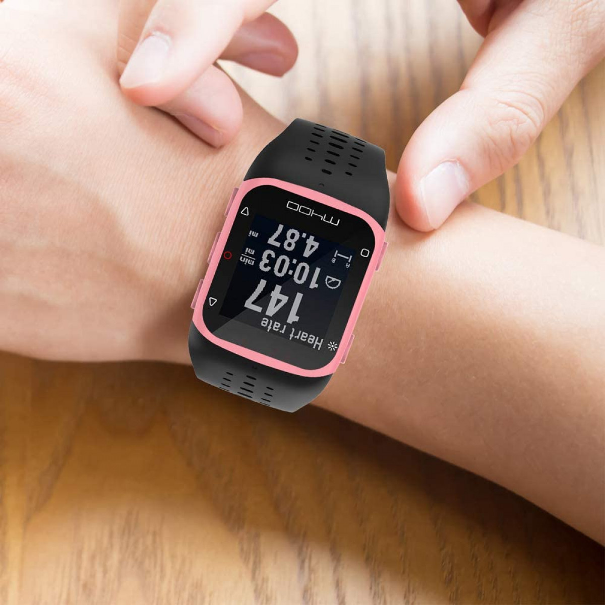 Eine schwarze Smartwatch an einem Handgelenk. Das Zifferblatt zeigt Daten: Zeit, Herzfrequenz und andere Metriken. Rosa Akzente sind sichtbar.