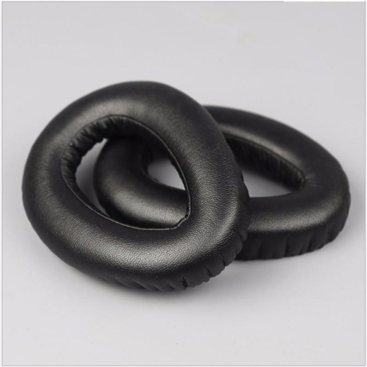 Dwie czarne, okrągłe nauszniki do słuchawek, obok siebie, na białym tle.