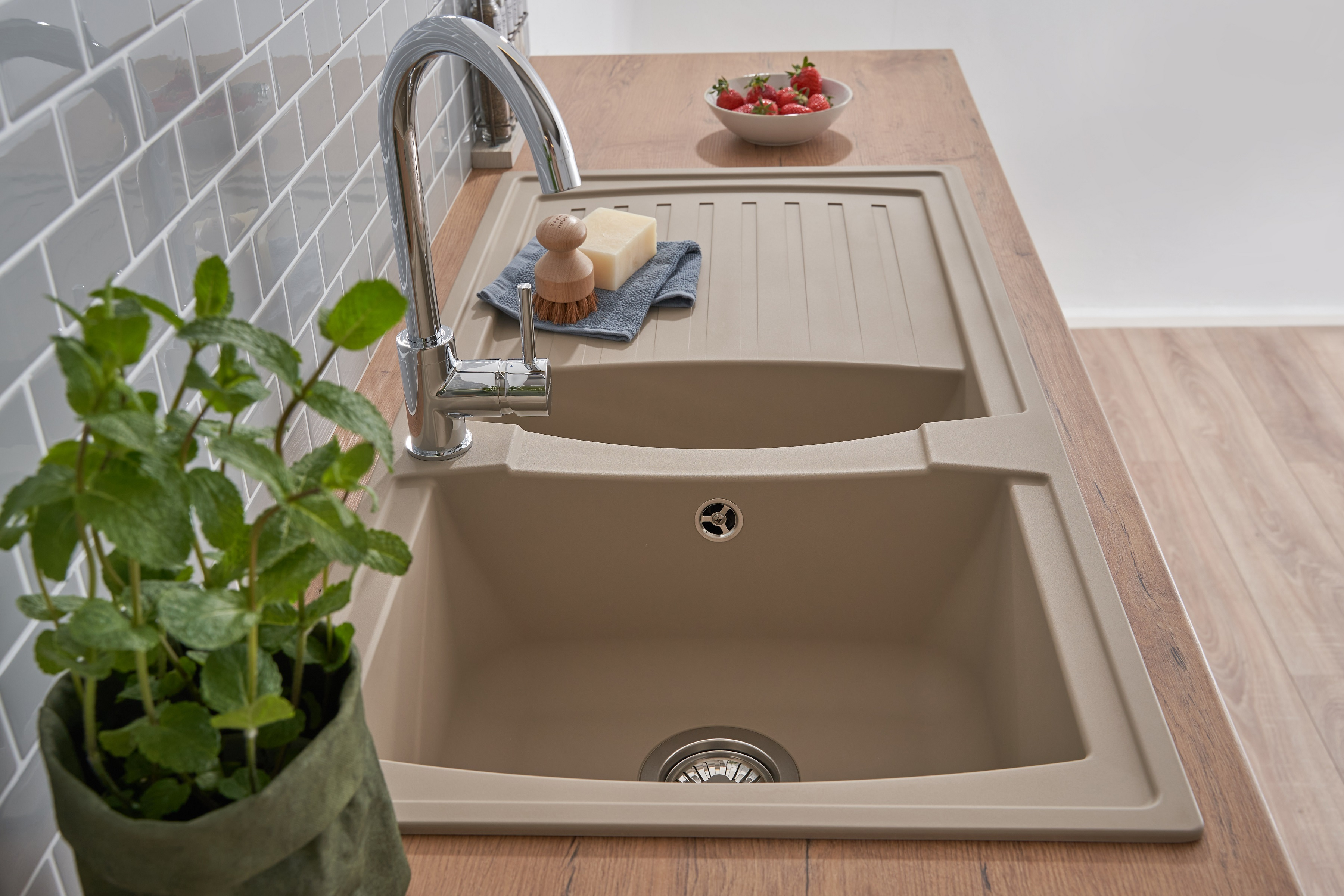 Küchenspüle mit Wasserhahn, Seife, Scheuerbürste und einer Pflanze. Erdbeeren in einer Schüssel.