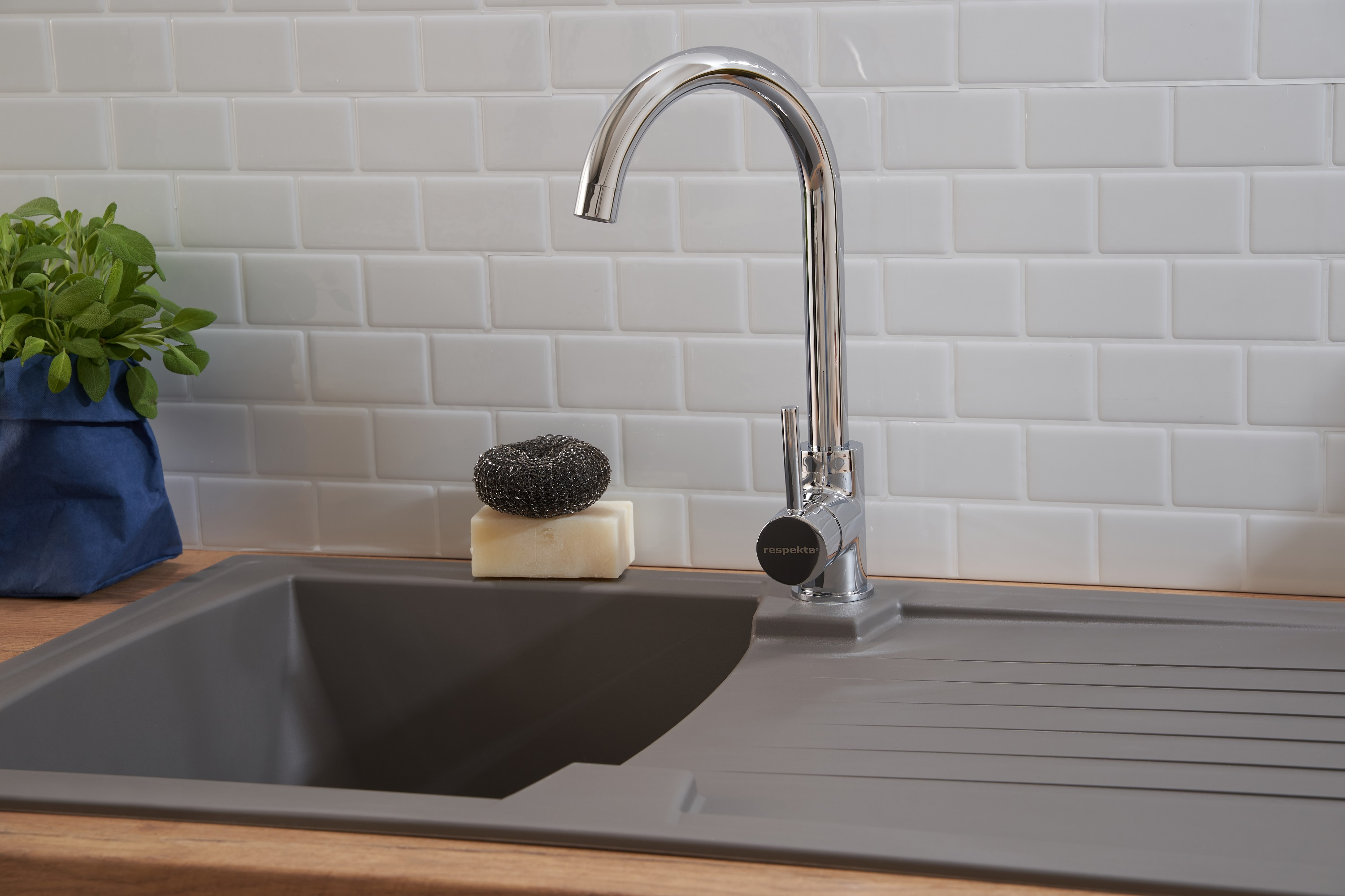 Ein Küchenbecken mit Wasserhahn, Schwamm und Seife sowie eine Pflanze im Hintergrund.