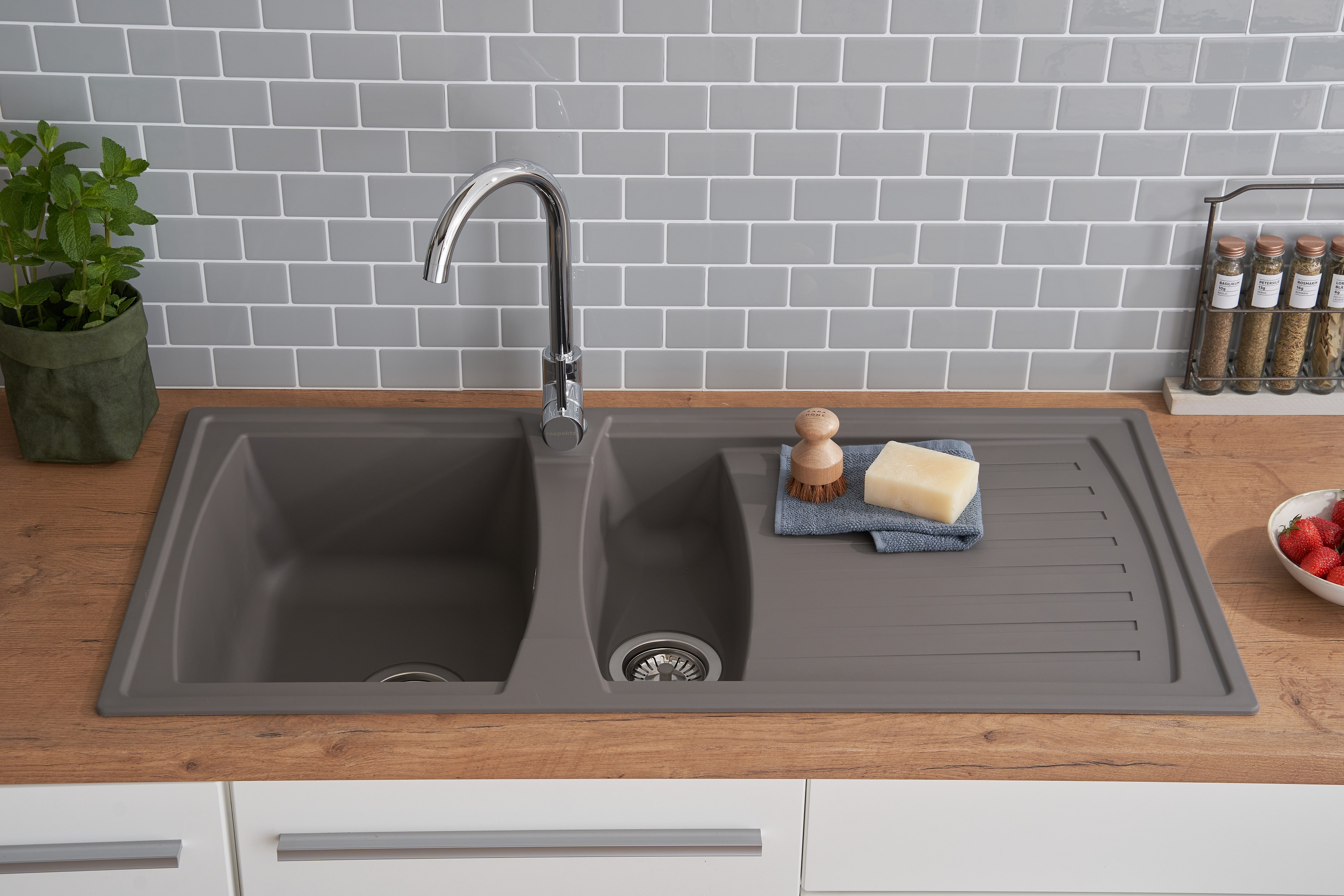 Küchenspüle mit zwei Becken und Wasserhahn. Eine Spülbürste, Seife und Erdbeeren liegen daneben.