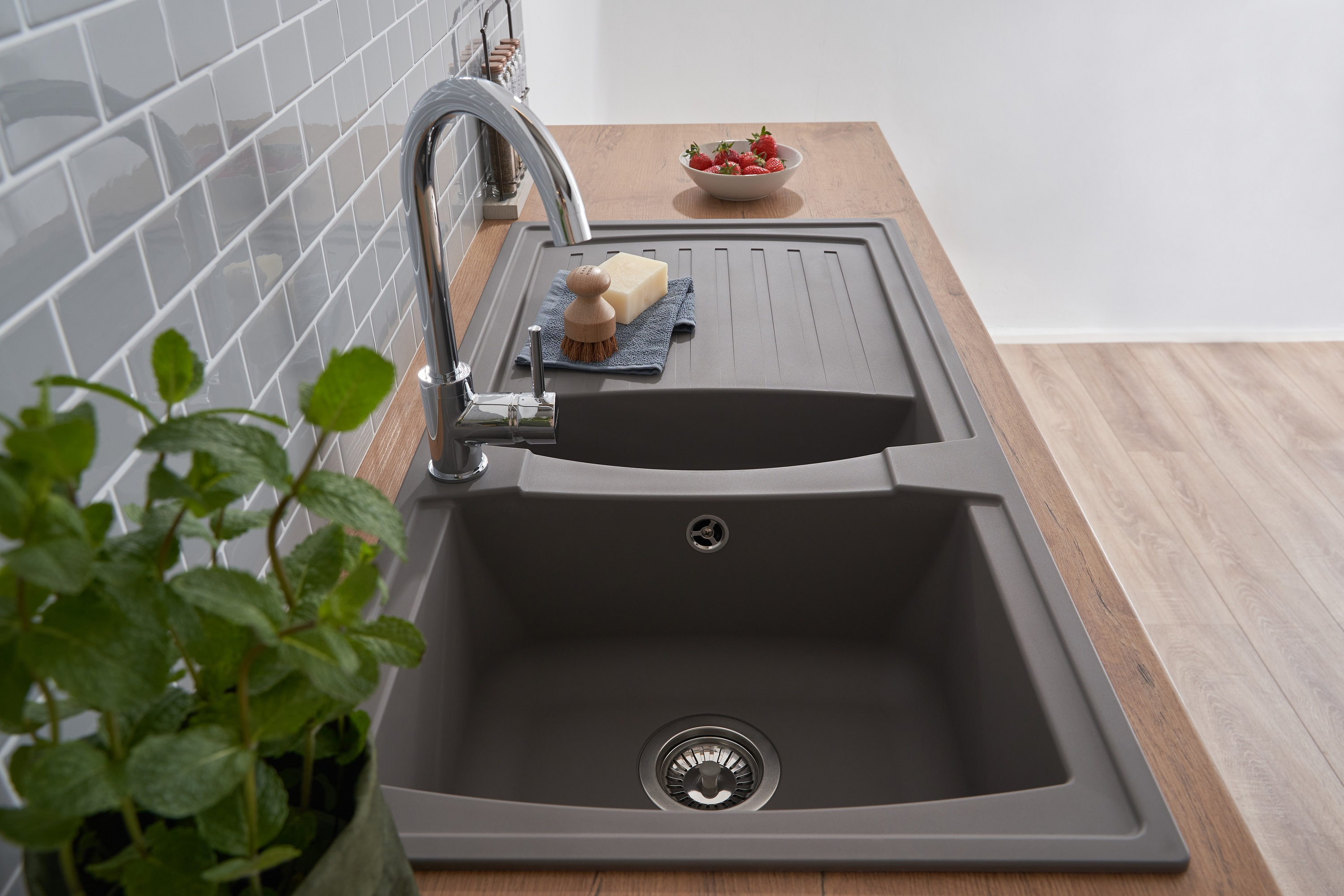 Ein Küchenwaschbecken mit Wasserhahn, einem Geschirrabtropfer und einer Schüssel Erdbeeren neben einer Pflanze.